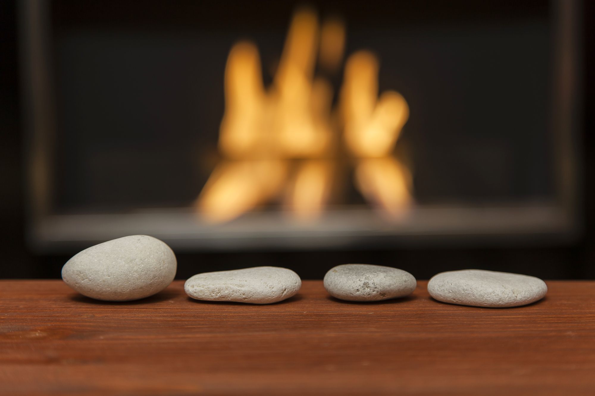 Four white pebbles are arranged in front of the fireplace on a wooden table. Indoor location with warm cozy feeling. Horizontal composition with lot of copy space.