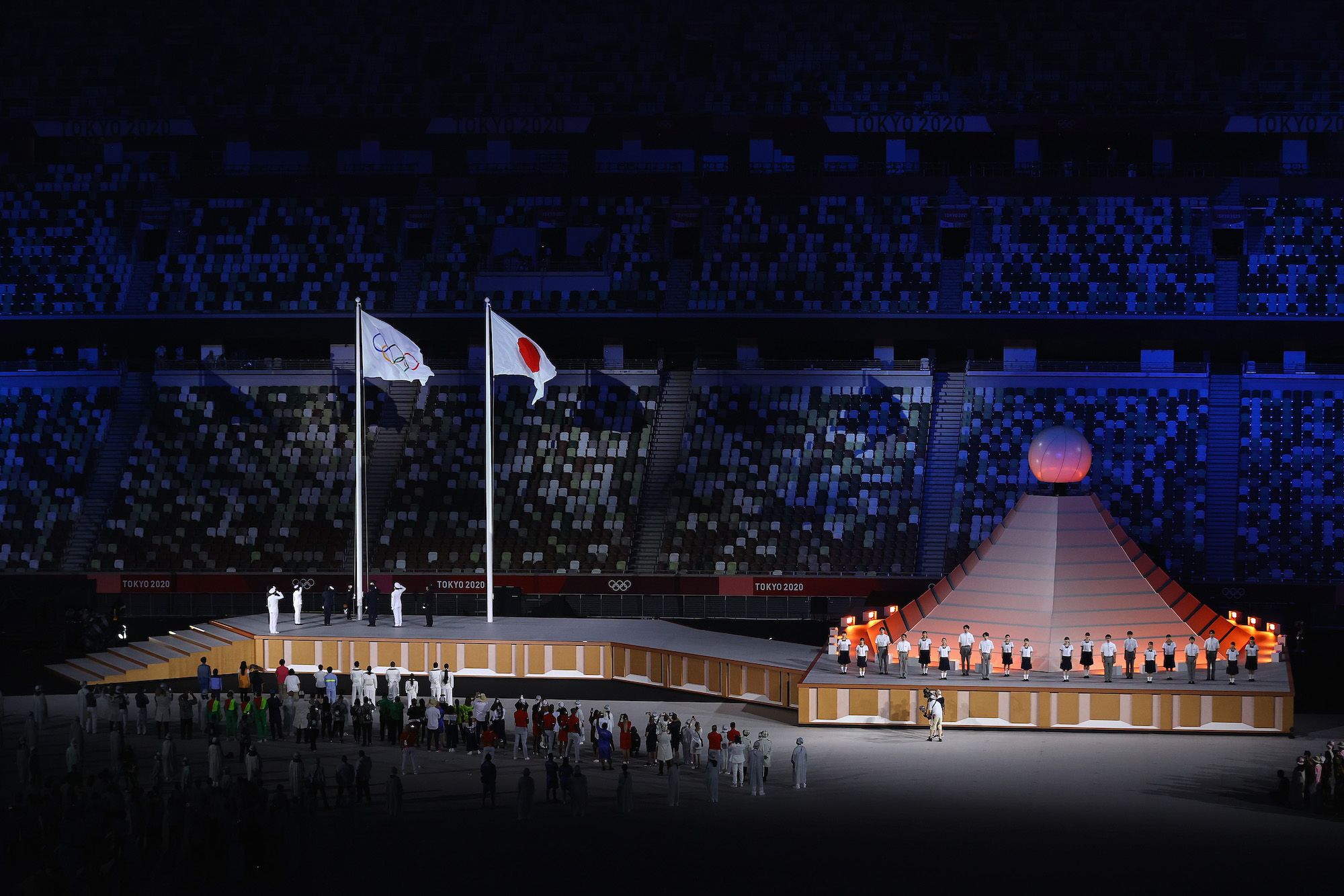 TOKYO, JAPAN - JULY 23: The Olympic flag is raised alongside the Japanese flag with the Olympic Cauldron during the Opening Ceremony of the Tokyo 2020 Olympic Games at Olympic Stadium on July 23, 2021 in Tokyo, Japan. (Photo by Laurence Griffiths/Getty Images)