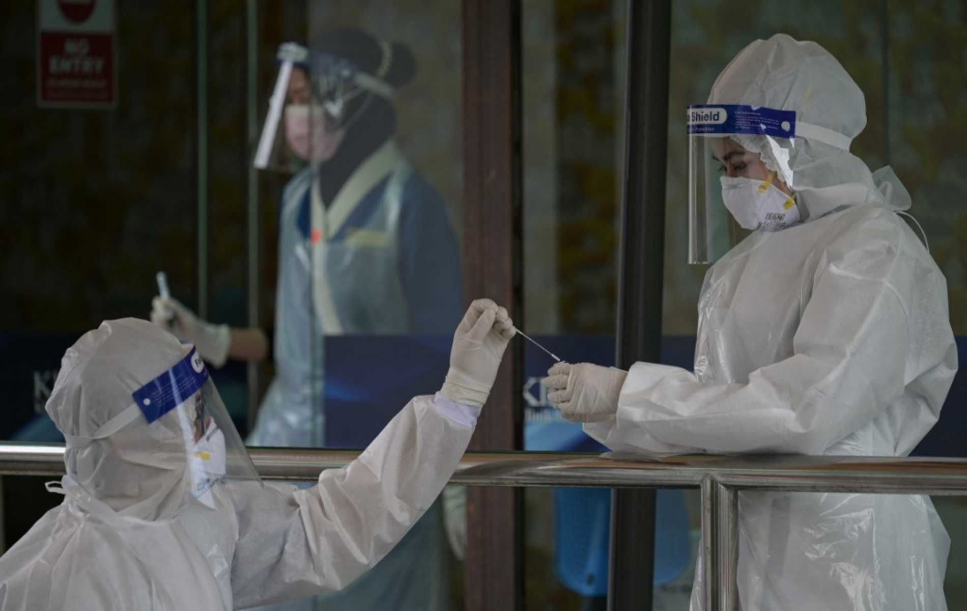 Medical personnel wearing protective suits conducts Covid-19 coronavirus test for people outside the Ajwa Private Clinic in Shah Alam on the outskirts of Kuala Lumpur on January 12, 2021, as Malaysia's king declared a nationwide state of emergency to fight a coronavirus surge. (Photo by Mohd RASFAN / AFP)