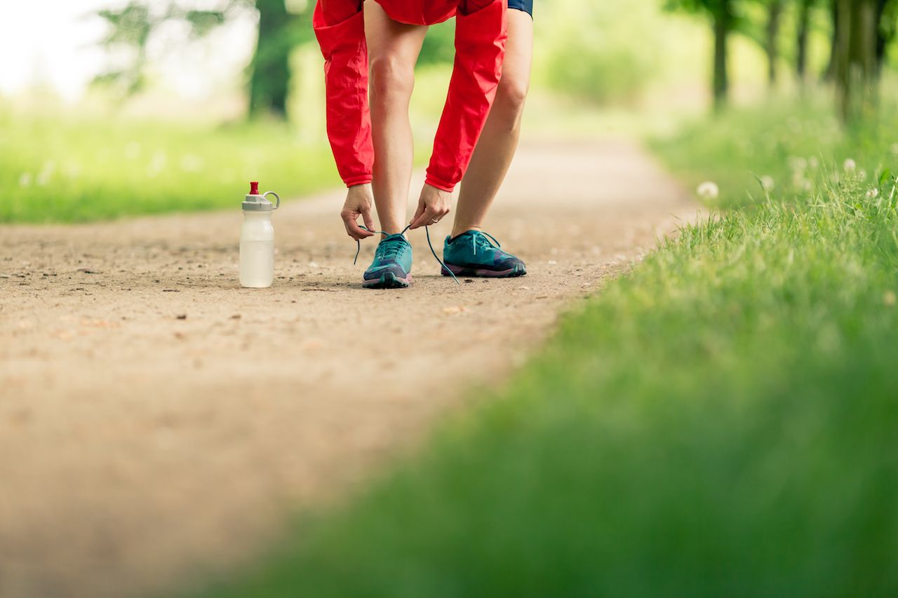 Woman runner tying sport shoes. Walking or running legs, autumn adventure and exercising outdoors. Motivation and inspiration fitness concept outside.