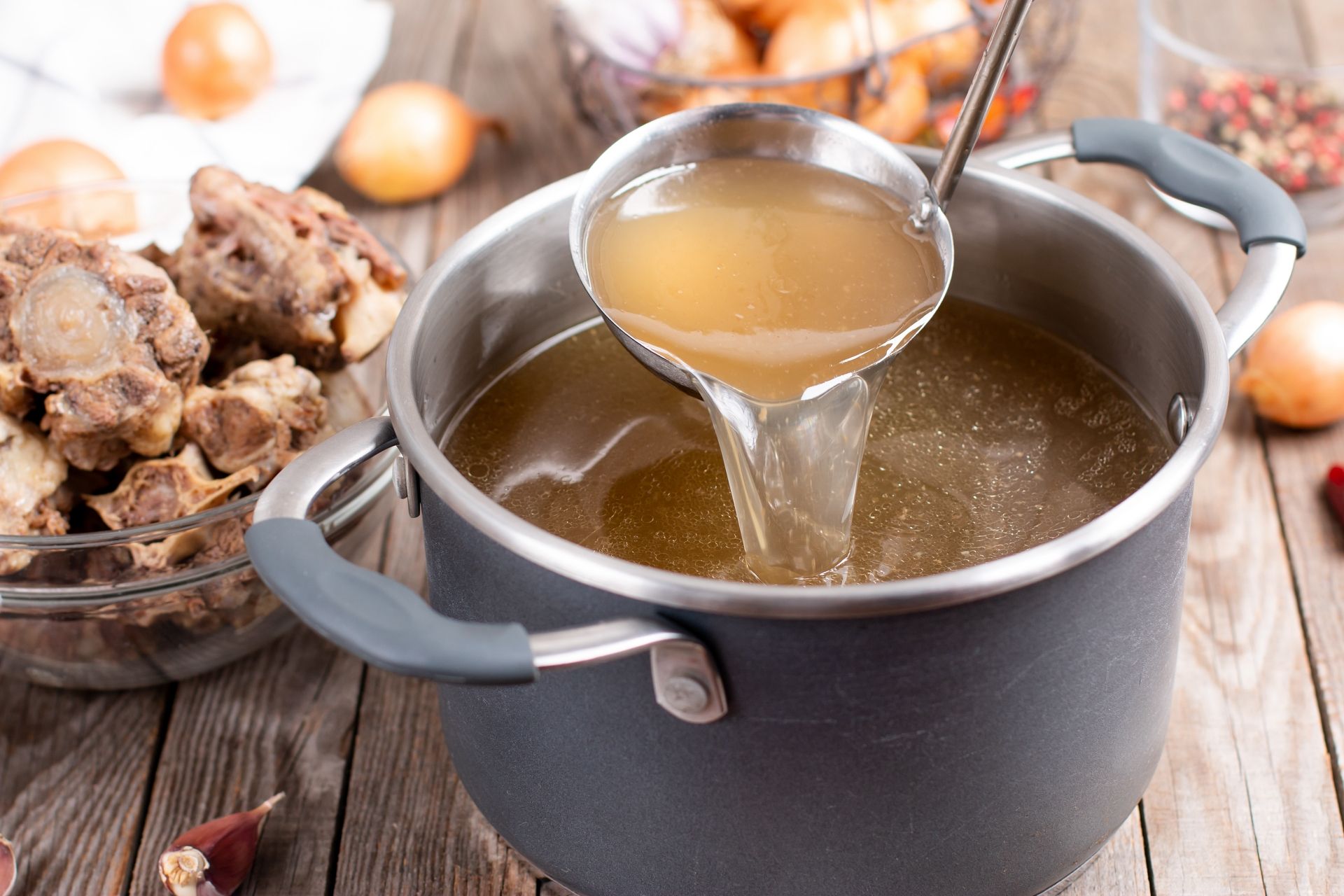 Saucepan with bouillon with a ladle on the table. Bone broth