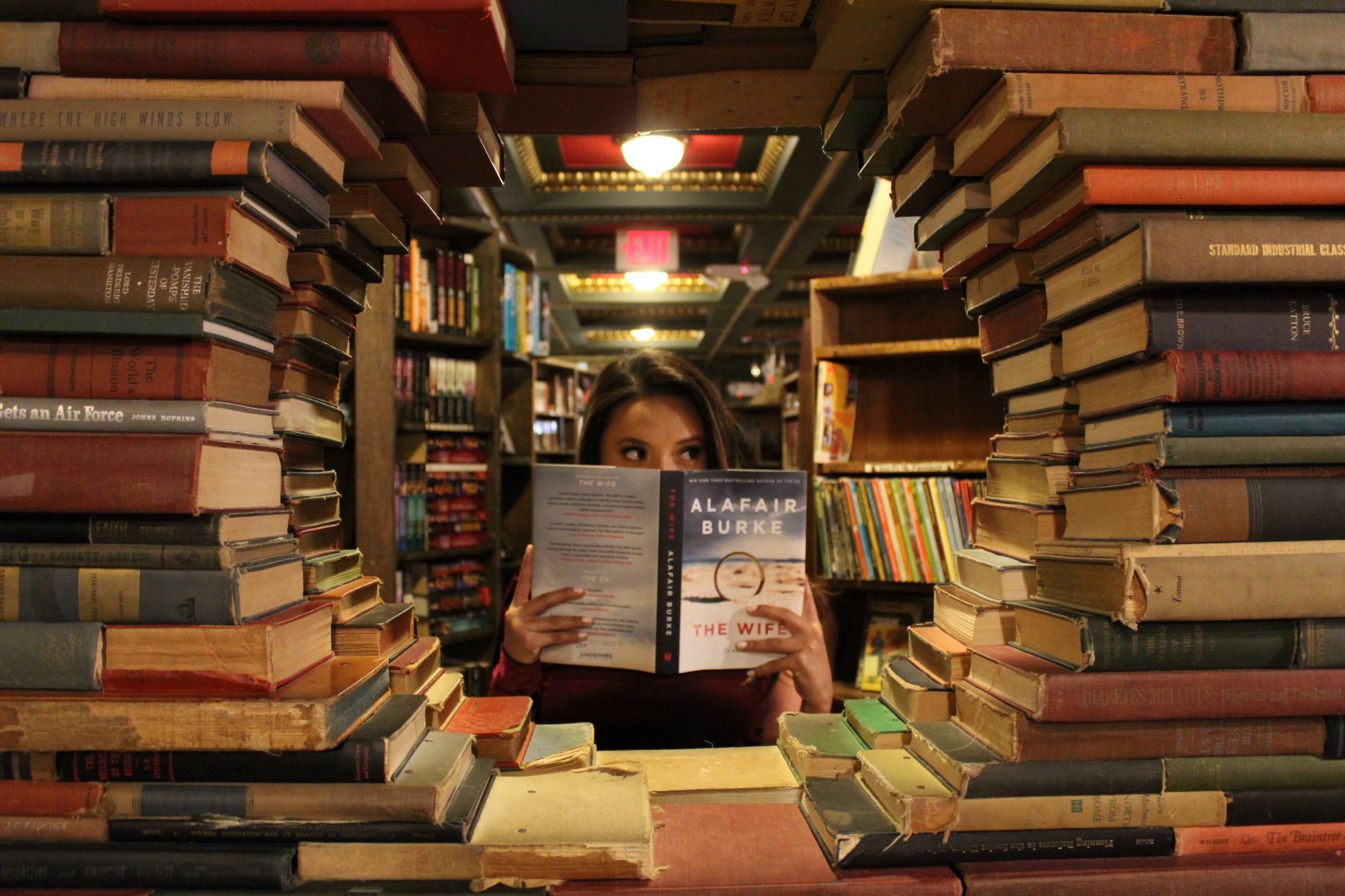 Woman lost in her imagination while surrounded by books inside a library. | Photo by Daniel on Unsplash