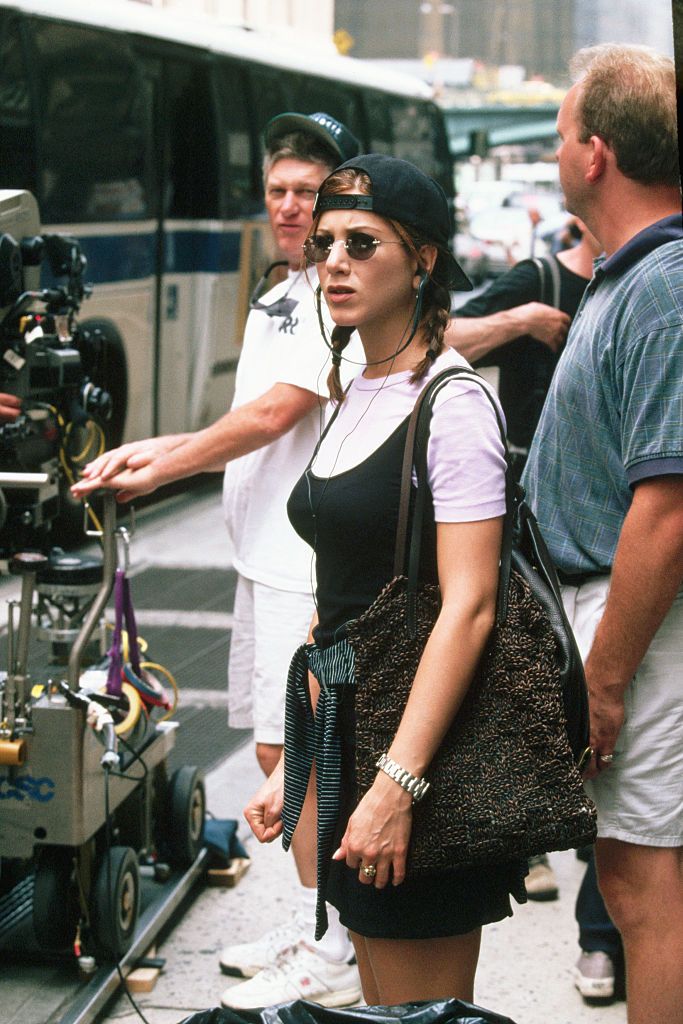 Wearing a backwards baseball cap and sunglasses, actress Jennifer Aniston stands on the set of the motion picture, Picture Perfect, during filming on the streets of New York City. (Photo by Mitchell Gerber/Corbis/VCG via Getty Images)
