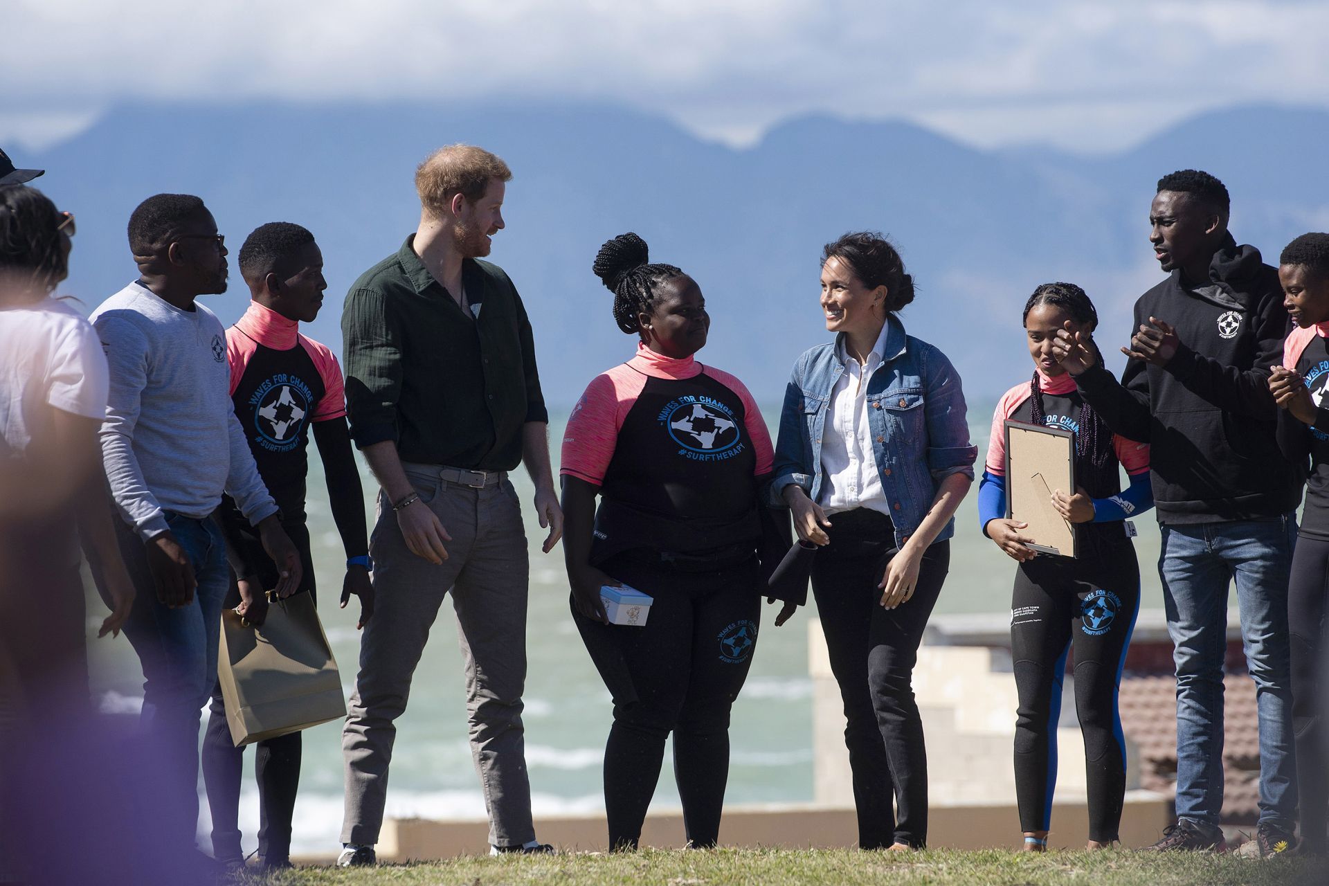 Prince Harry (4thL), Duke of Sussex and Meghan (4thR), Duchess of Sussex, meet members of "Waves For Change" NGO at Monwabisi Beach outside of Cape Town on September 24, 2019. - "Waves For Change" NGO fuses surfing with child-friendly mind and body therapy to provide mental health services to vulnerable young people living in challenging communities. (Photo by DAVID HARRISON / AFP)