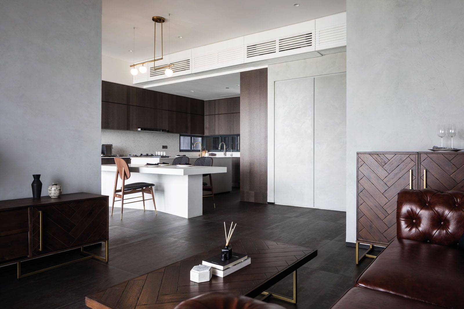 The herringbone pattern on a cabinet and coffee table in the living room is echoed by the stitching details on the leather chairs in the kitchen