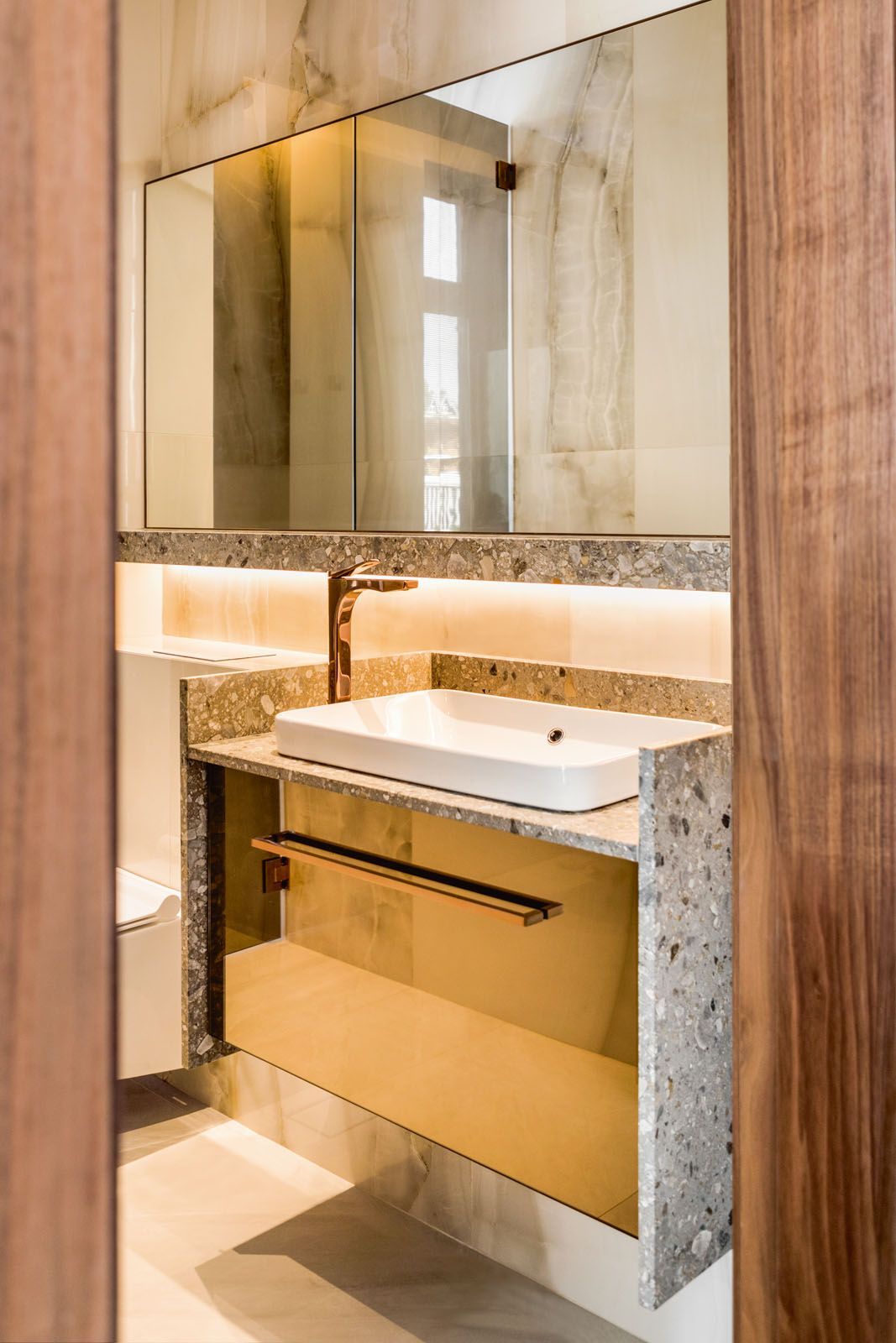 This powder room features rose gold Gessi taps as well as terrazzo and tinted mirror panels on its vanity counter