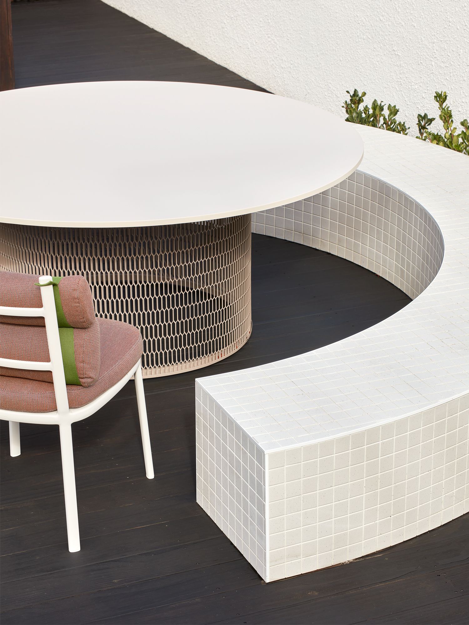 The C-shaped outdoor bench curves around the Kettal Mesh table and Roll armchair