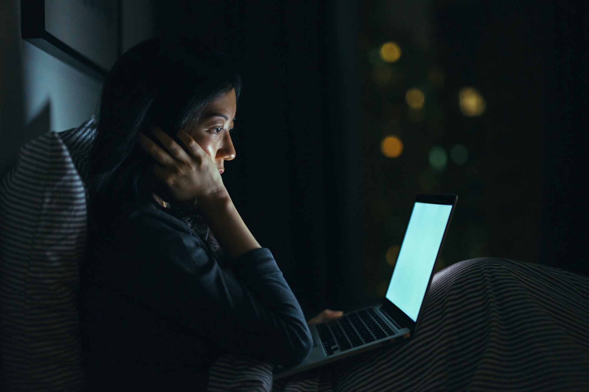 Young woman in deep thought while using laptop on bed at night