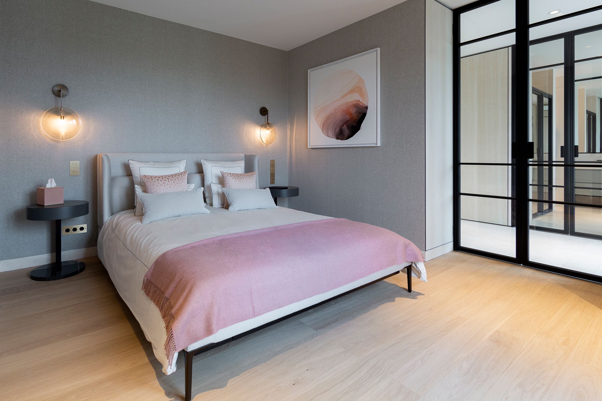 Glass doors custom designed by Rinderknecht offers a peek into the bedroom, which features a Joyce Niche bed from Wittmann, Ralf bedside tables by Meridiani, and an artwork by Ilaria Franza