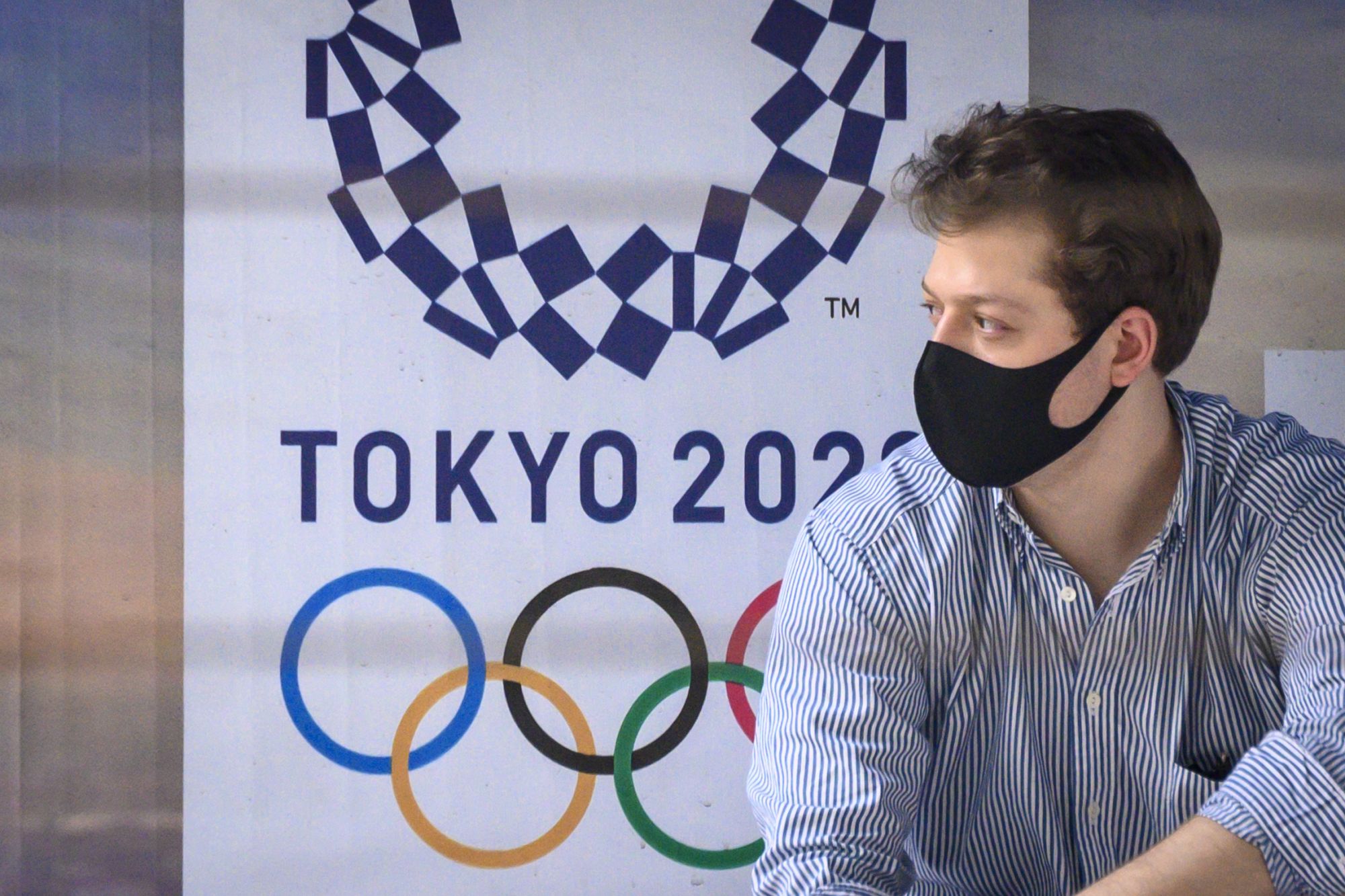 A man wearing a facemask, amid concerns over the spread of the COVID-19 coronavirus, sits at a bus stop in front of a Tokyo 2020 Olympics advertisement in Bangkok on March 16, 2020. (Photo by Mladen ANTONOV / AFP)