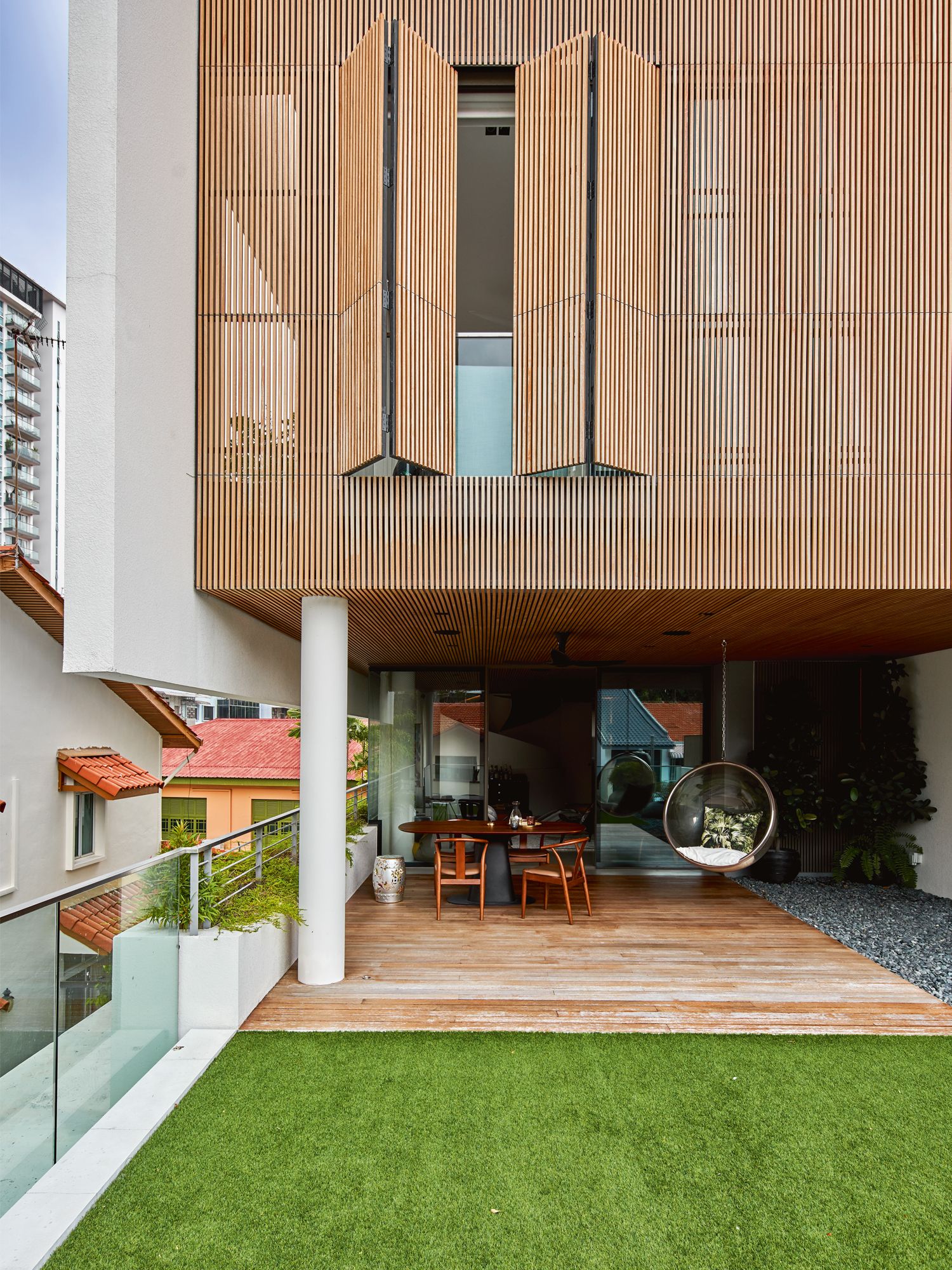 The slatted timber on the facade also extends inwards to the ceiling of the balcony and the indoor lounge; the swing chair at the balcony is styled with a cushion from Pierre Frey