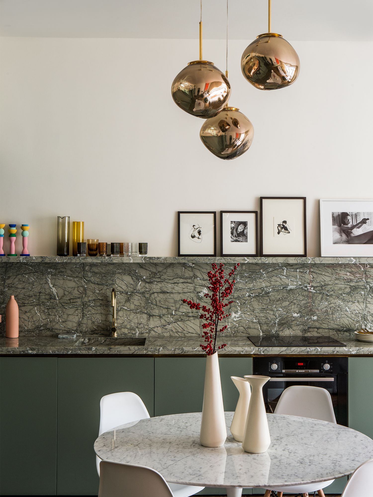 The kitchen features brass elements such as a spherical hanging light from Tom Dixon, which floats above a dining area featuring a Saarinen circular table and chairs from Eames