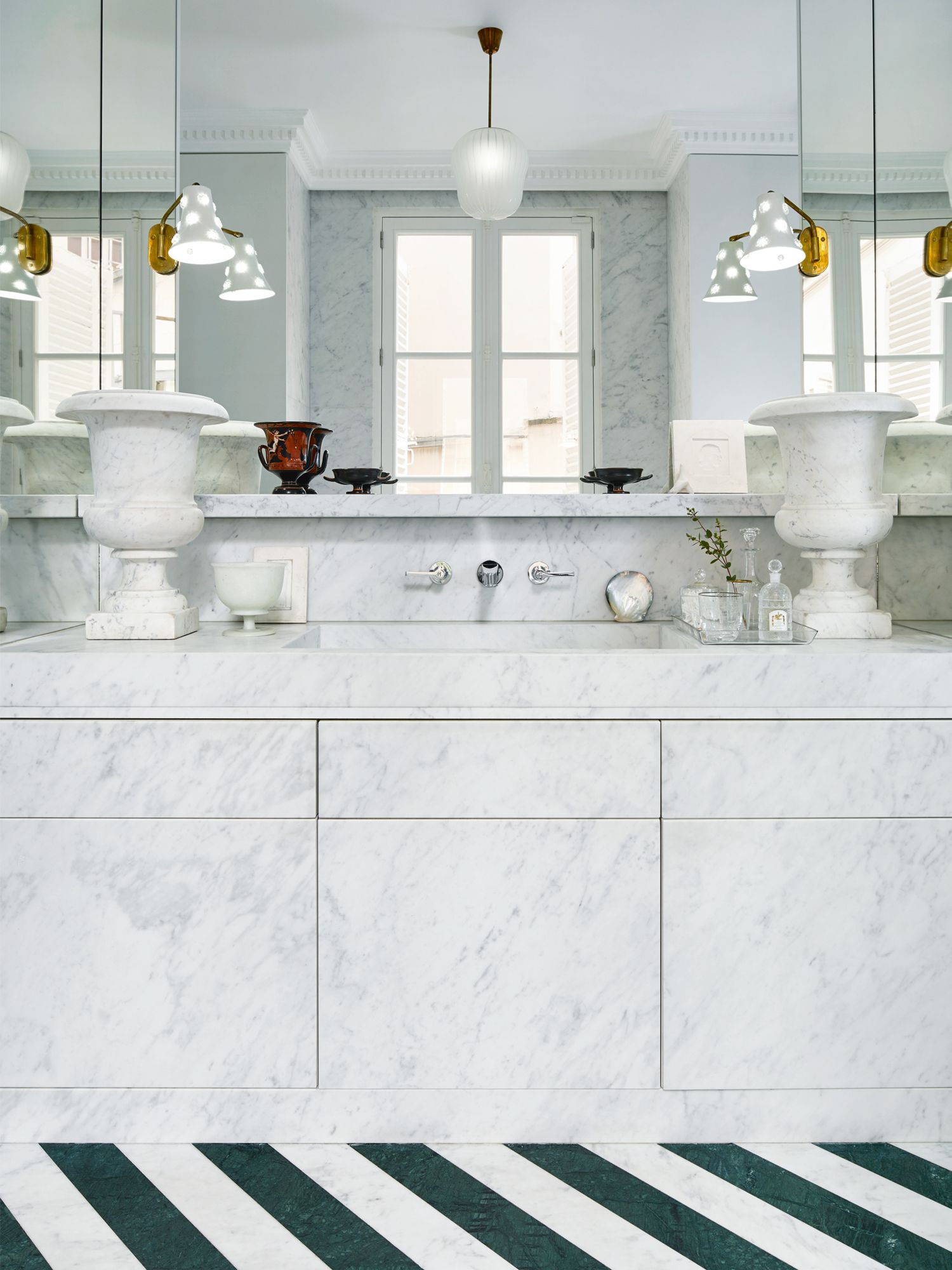 Luxuriously clad in Carrara marble, the master bathroom features sconces designed in Italy from the seventies and a pair of antique Greek vessels