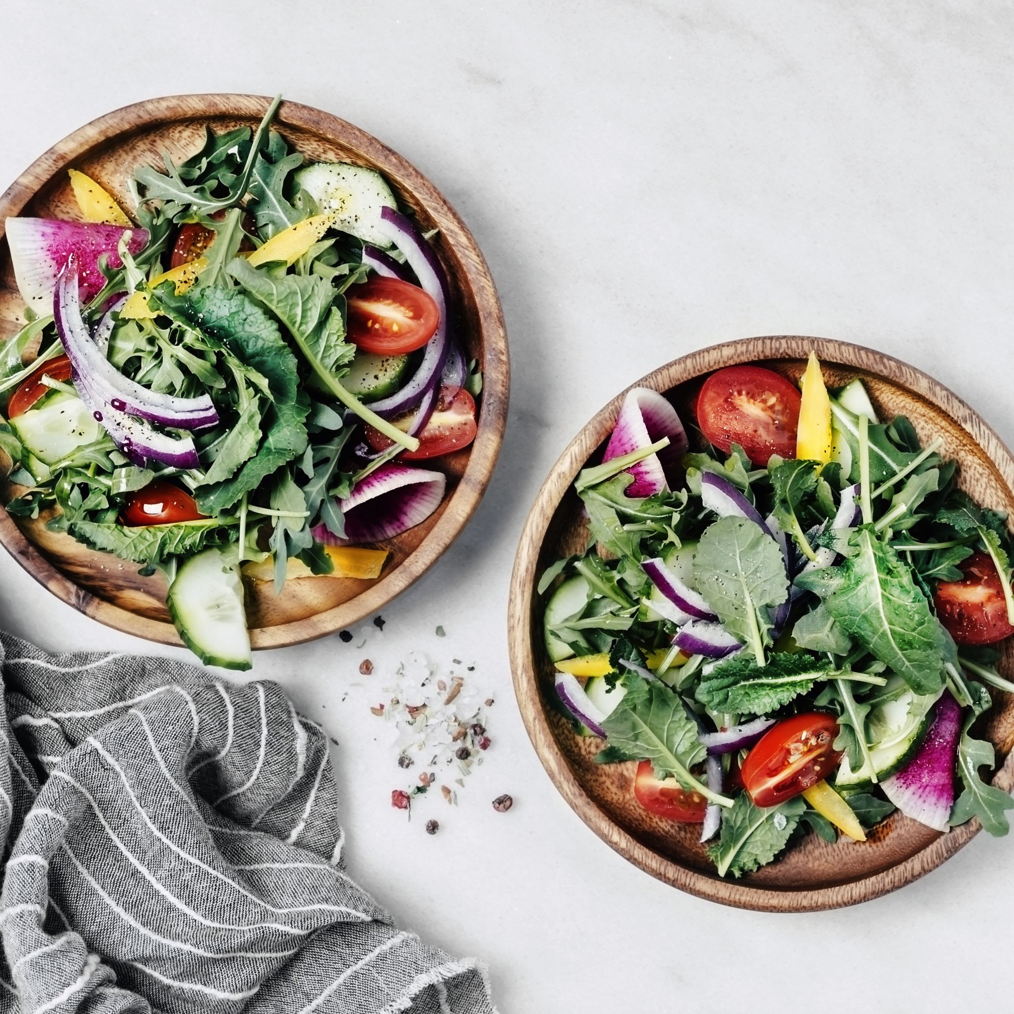 Two plates of fresh arugula and baby kale salad on white background