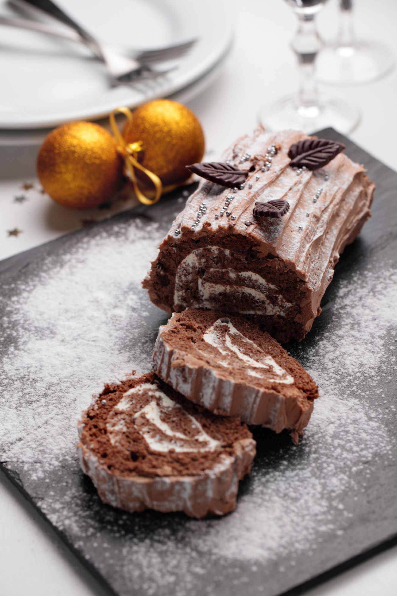 Yule log cake decorated with chocolate leaves on a Christmas table