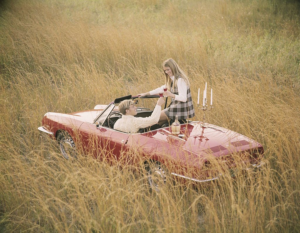 Romantic couple in sports car convertible enjoying wine in field