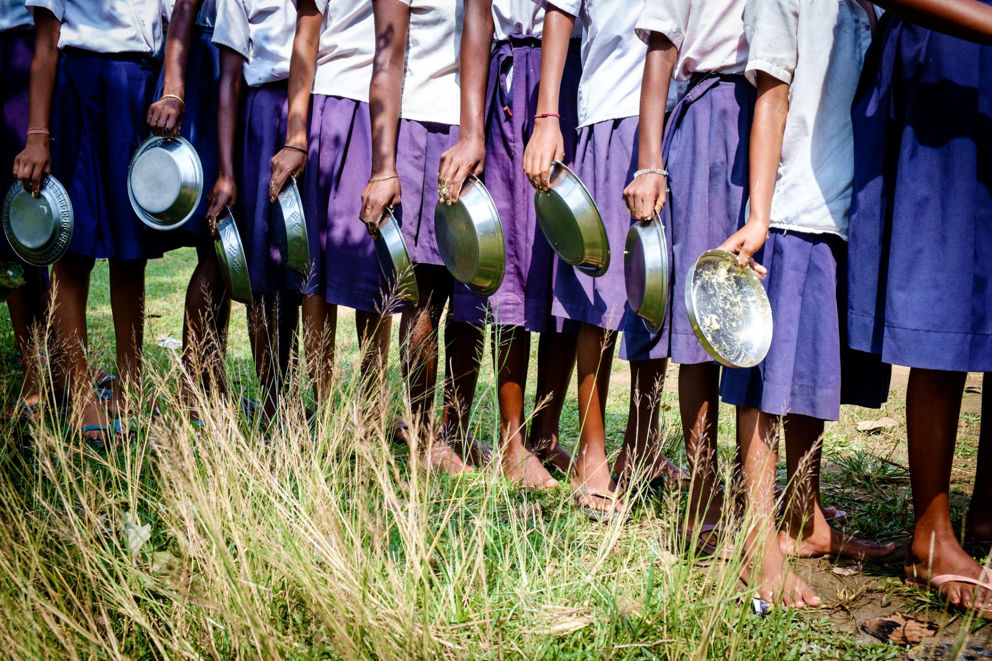 A group of girl school children queued up to wash their utensils after finishing their mid day meal.
