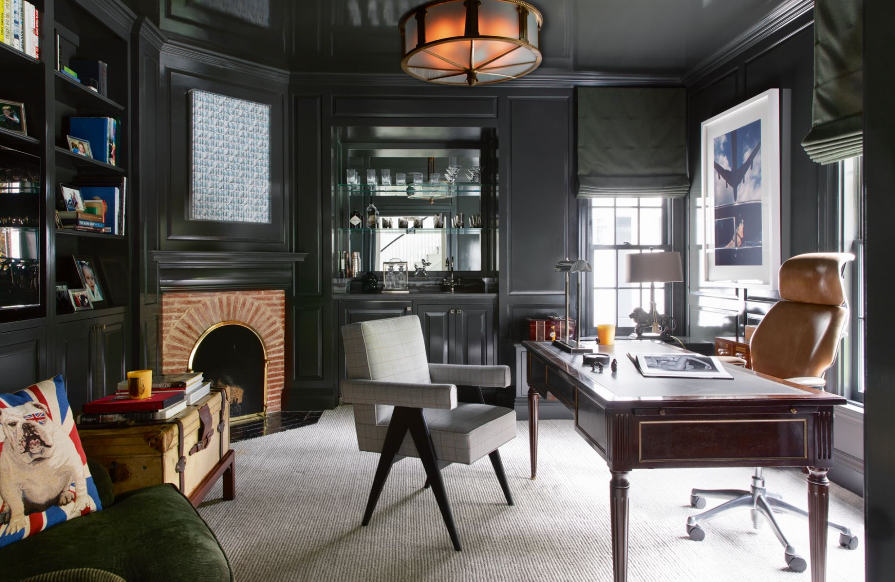 Black cabinetry and walls create a cocooning effect in the study, which also features a vintage bronze chandelier, a sofa in hunter green upholstery and a brick fireplace