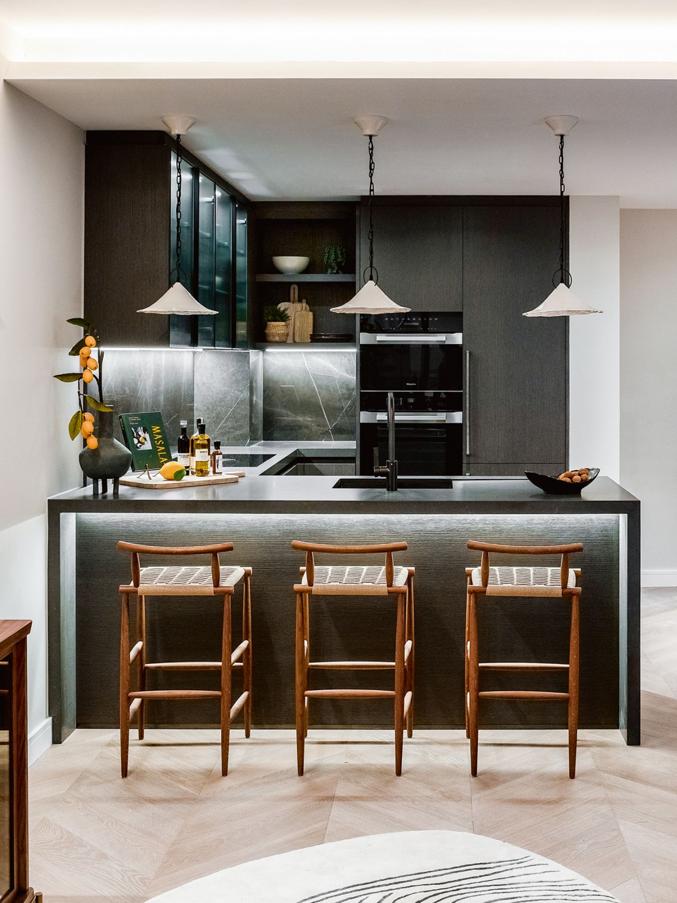 In the kitchen, the cool grey anthracite stone countertop is juxtaposed with the wooden warmth of the Pelleossa bar stools by Francesco Faccin from Miniforms