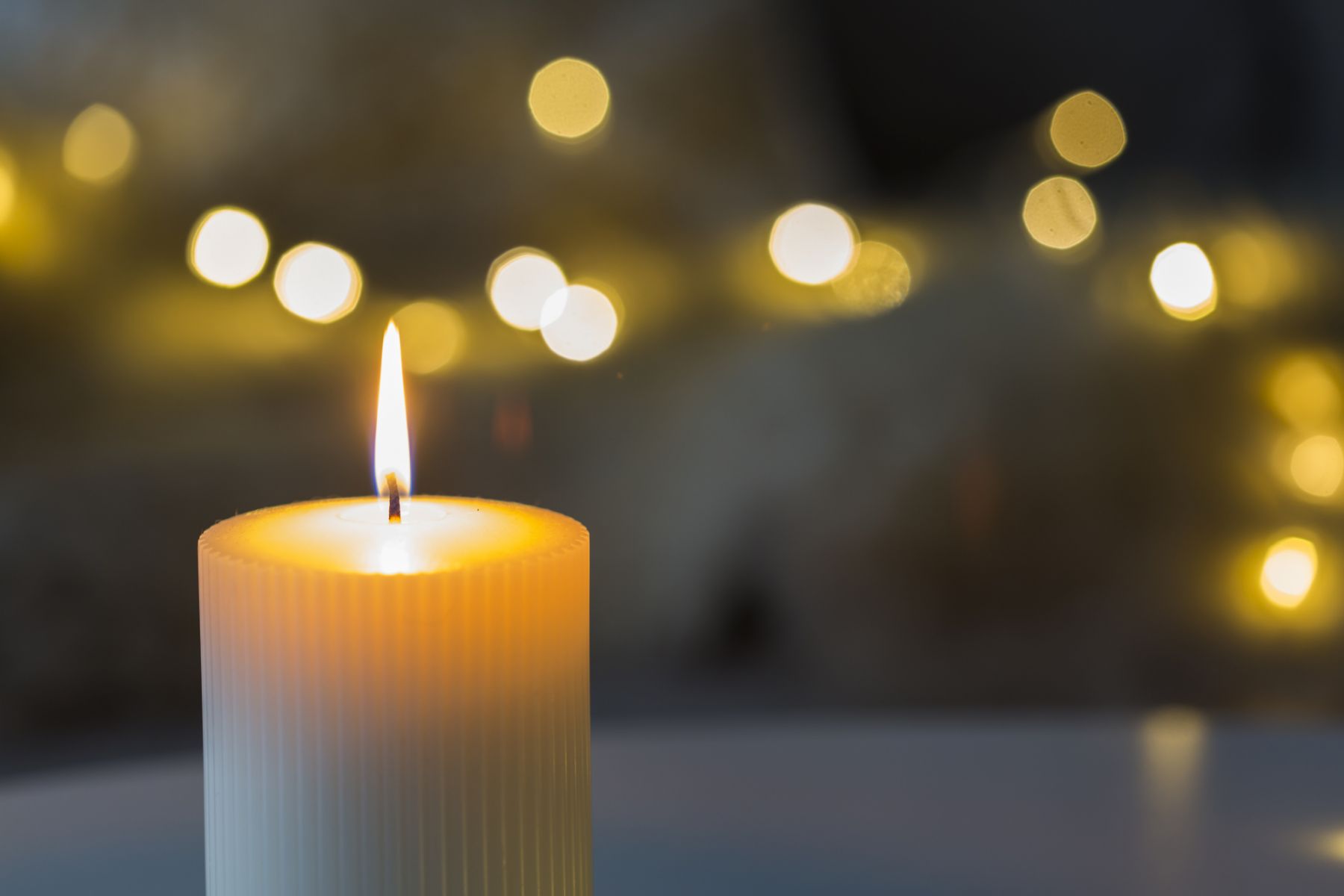 Festive background with burning cylindrical white candle in the foreground and bokeh of sparkling party lights in the background with copy space