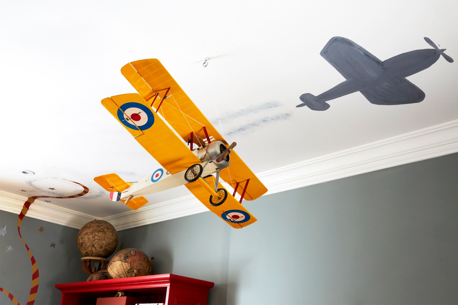 The plane model hanging from the ceiling features a hand-painted mural of sticker tape trailing behind, adding both pattern and a sense of adventure to the space