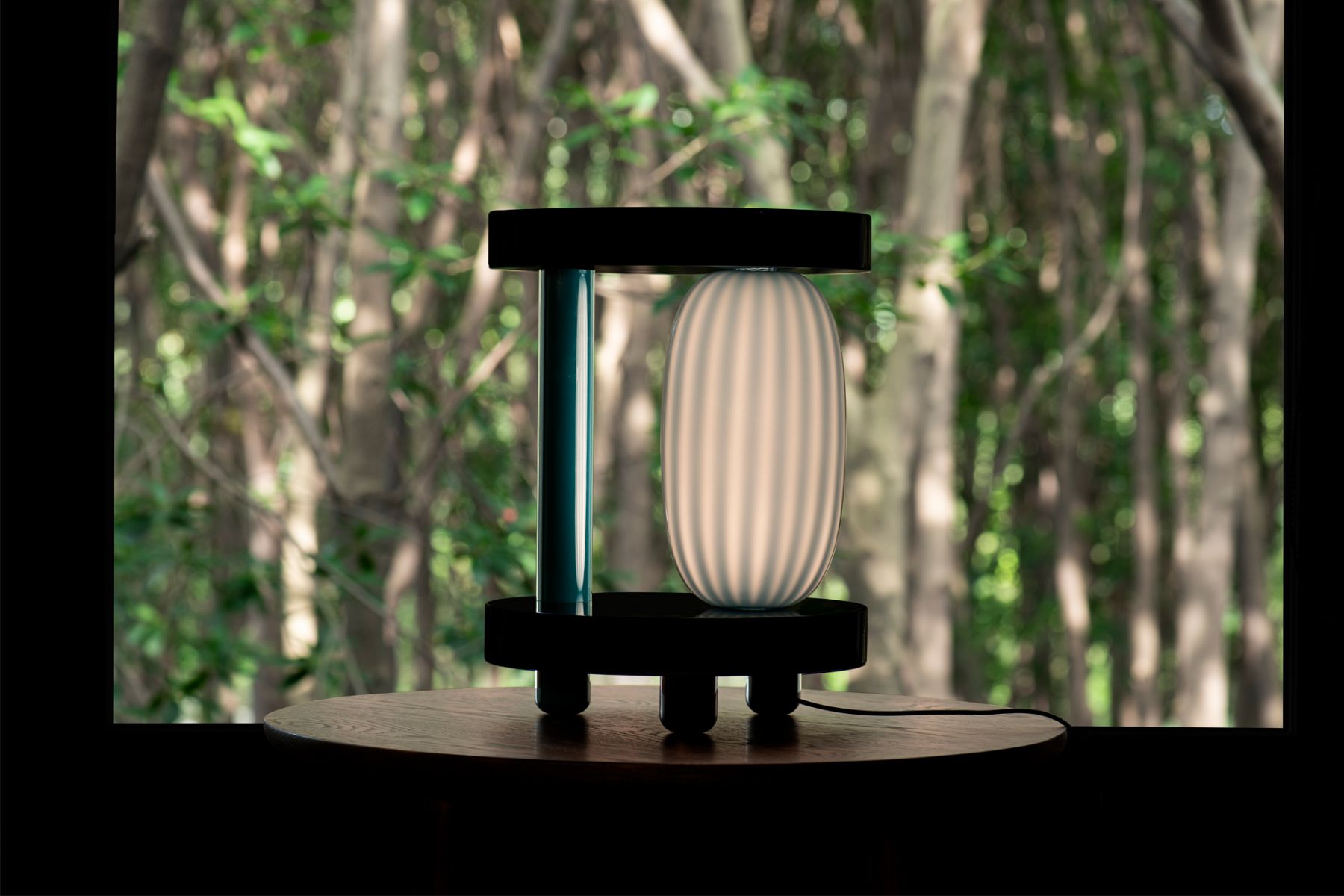The Hoba side table and lamp features a minimalist circular base that's carrying a  Murano glass shade and supported by discreet legs