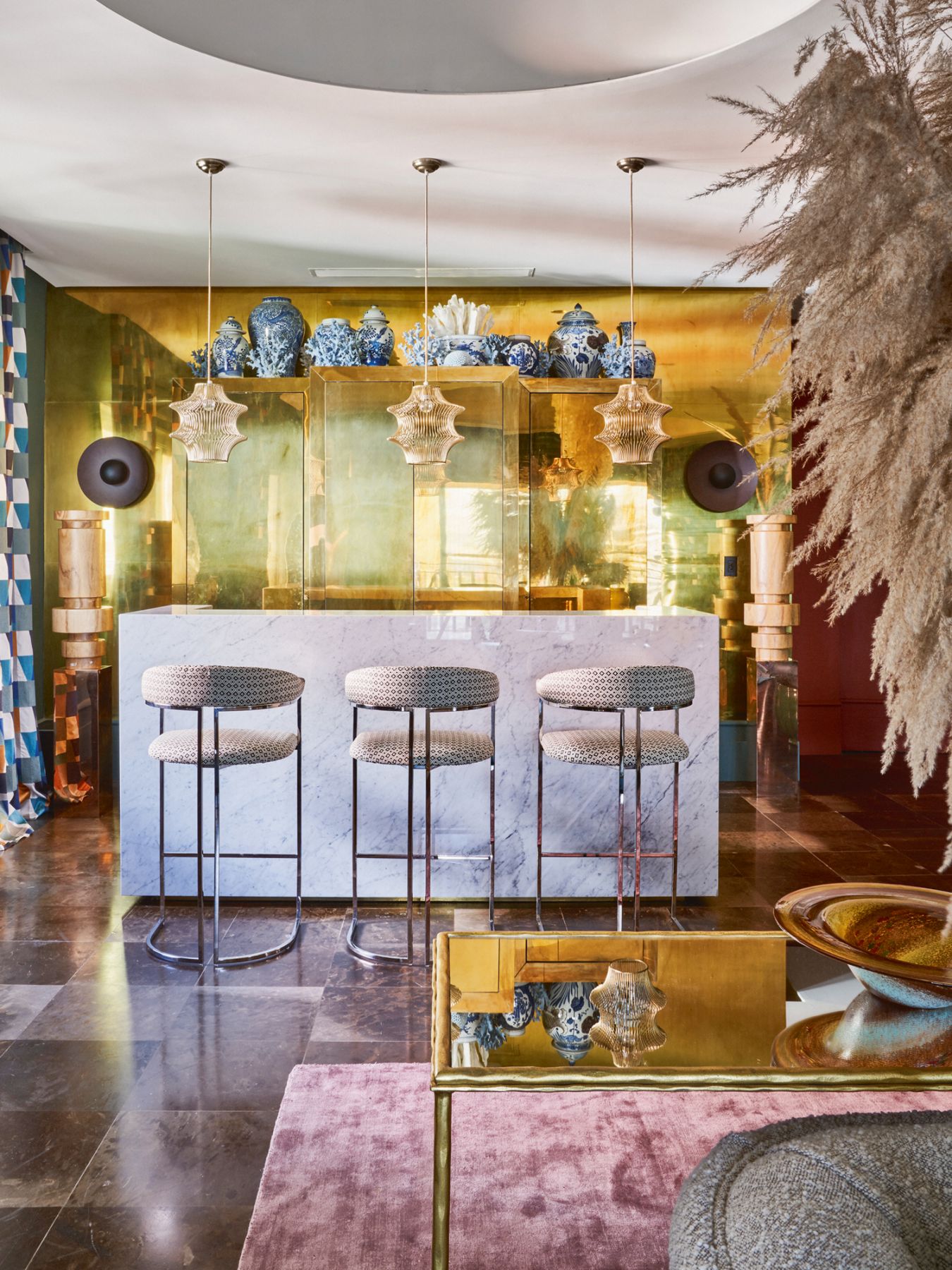 The bar area features a Carrara marble island, raffia upholstered armchairs, wall sconces by Aromas del Campo, and a collection of Chinese vases from Ilume