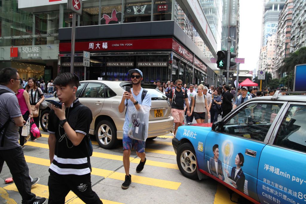 Lots of people at an intersection cross the street on a crossroad, some use their smartphones, they are walking between cars that did not make the green light before it turned red, Nathan Street, Kowloon, Hong Kong, China, May 7, 2016. (photo by Dan Porges/Getty Images)