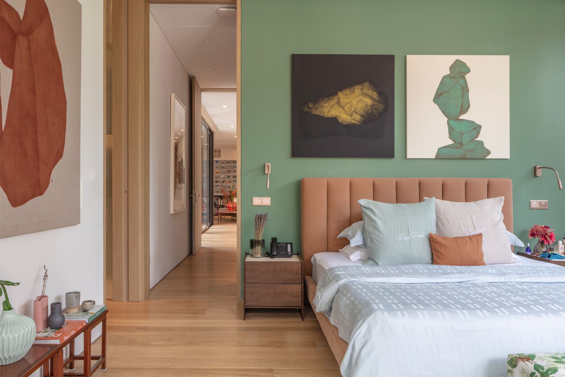 A green feature wall in the master bedroom is complemented by contrasting artworks and a tan headboard
