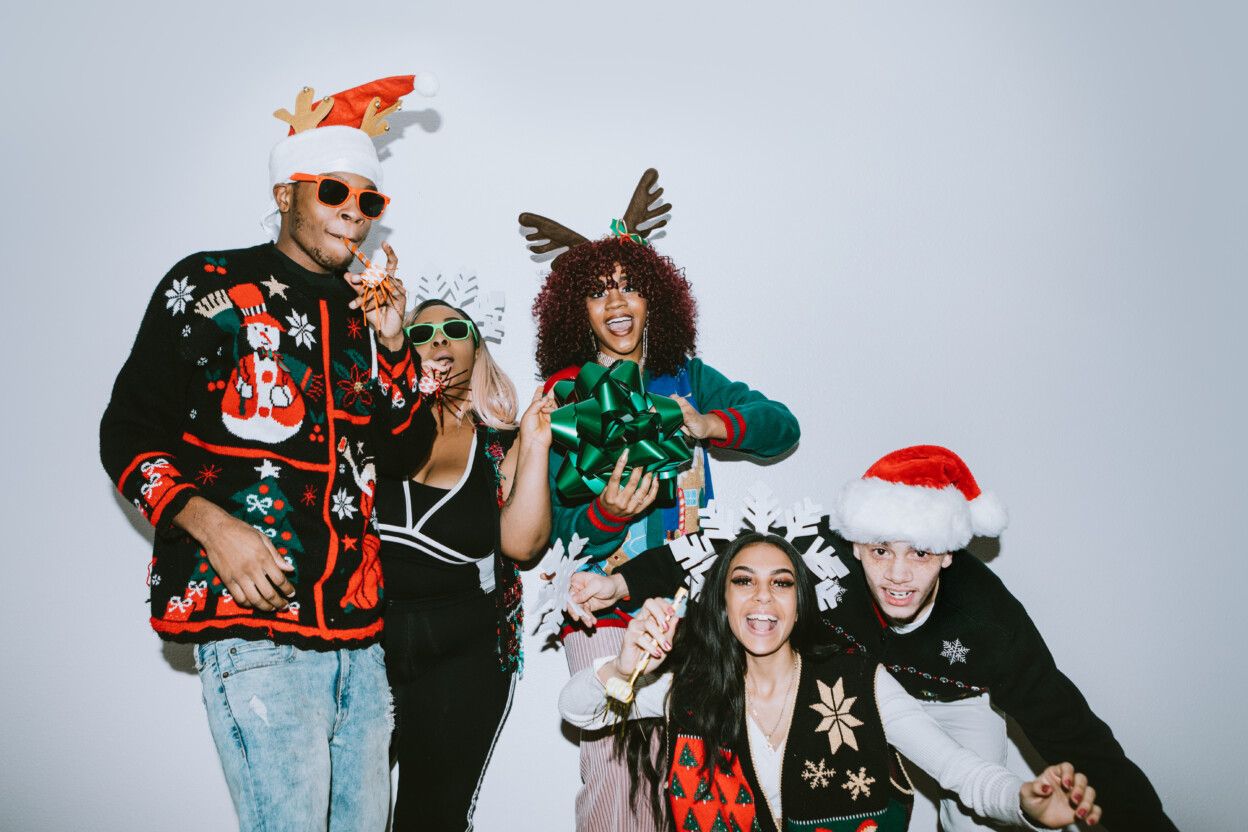 A group of young adult friends gather at a home for Christmas celebration over the holiday, dressed to fit the occasion with various Christmas accessories and ugly sweaters.  They pose for some photos, direct camera flash.