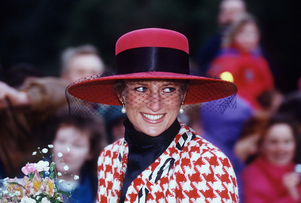 SANDRINGHAM, UNITED KINGDOM - DECEMBER 23: Diana, Princess Of Wales, Smiling On A Walkabout After Attending Christening Service At Sandringham Church. The Princess Is Wearing A Houndstooth Red And White Jacket Designed By Moschino With A Black Polo Neck Jumper And A Broad-brimmed Red Hat. (Photo by Tim Graham Photo Library via Getty Images)