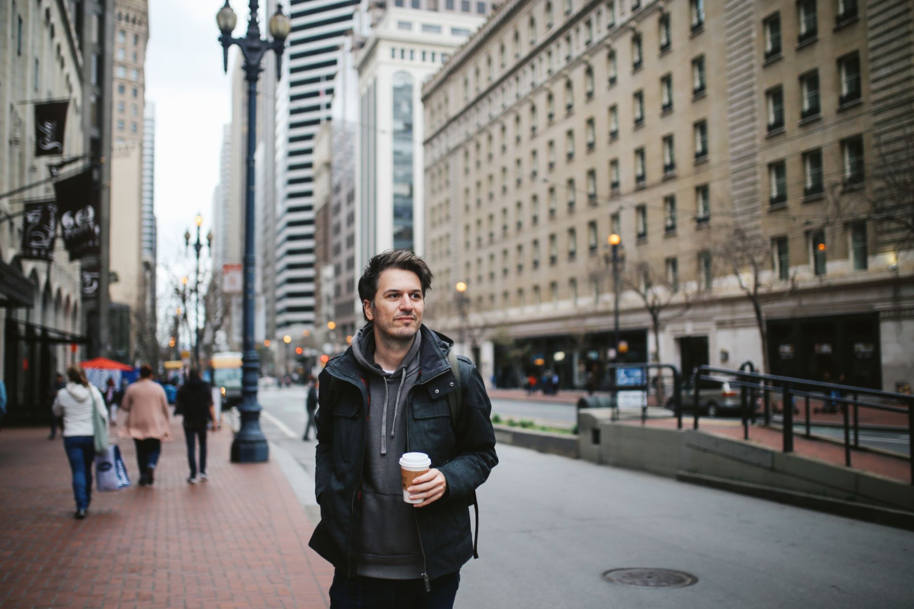 Young man working in the vibrant Silicon Valley IT scene standing on the sidewalk in San Francisco, downtown district, having a coffee break.