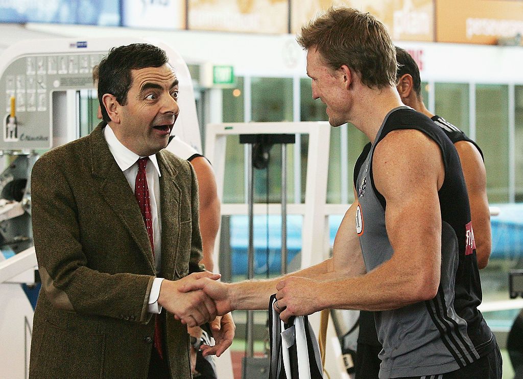 MELBOURNE, AUSTRALIA - MARCH 09: Actor Rowan Atkinson in character as Mr. Bean shakes hands with Nathan Buckley of the Magpies during the Collingwood Magpies AFL gym training session at the Lexus Centre on March 9, 2007 in Melbourne, Australia. (Photo by Quinn Rooney/Getty Images)