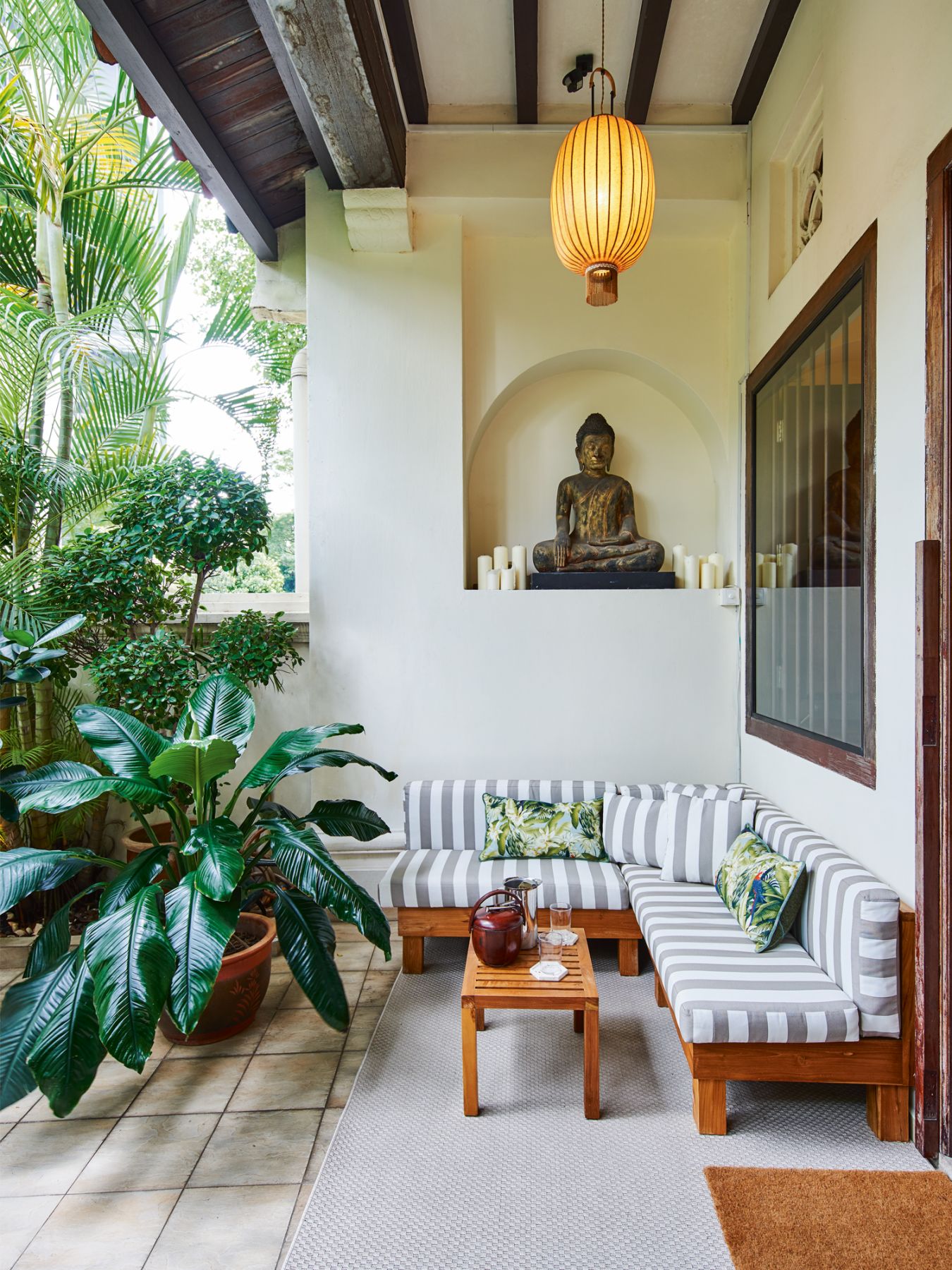 Lush foliage adds a verdant layer to the entryway, which also features custom outdoor furnishings from Rooma, and is styled with cushions from Pierre Frey