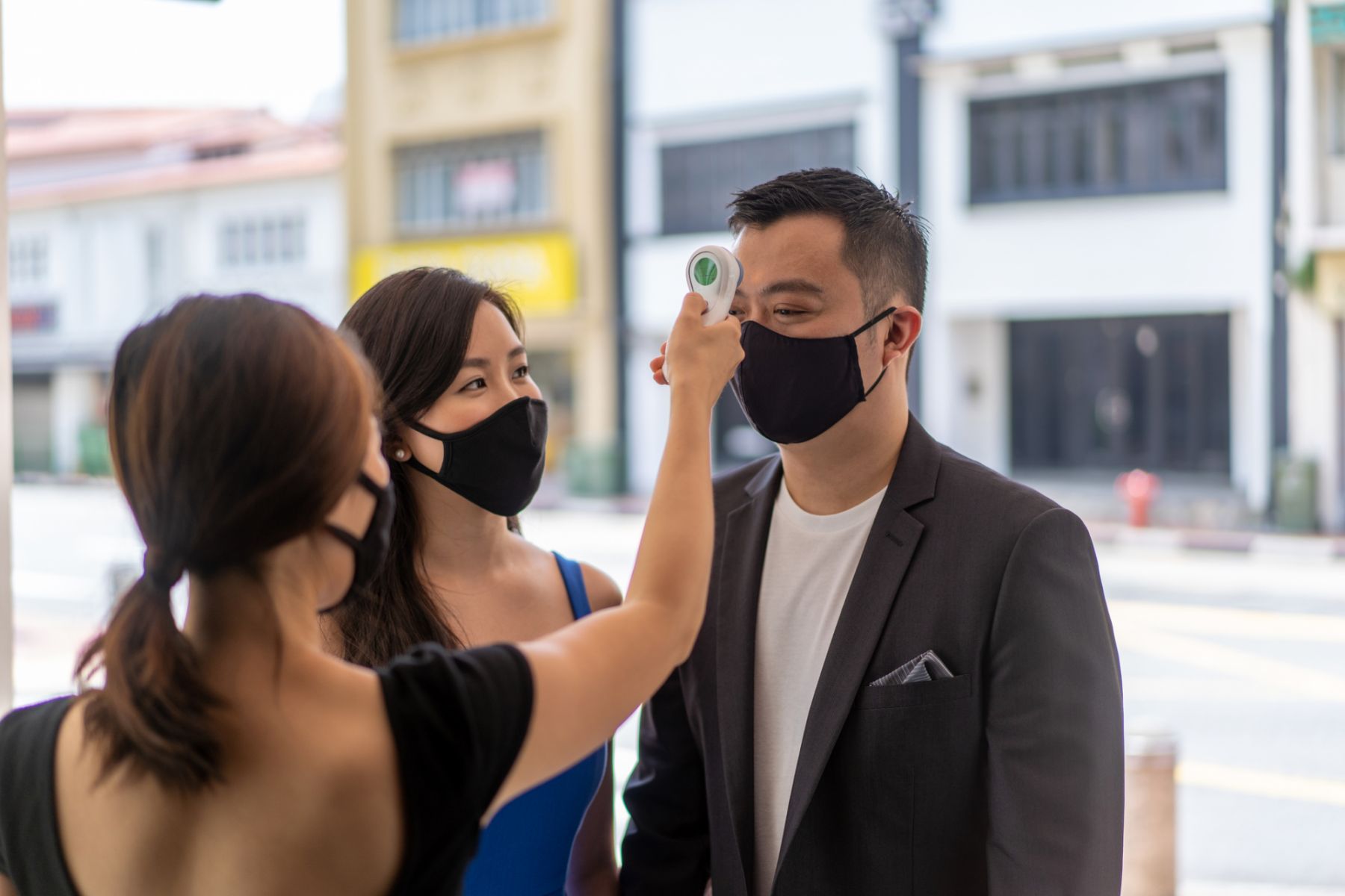 Asian waitress taking temperature of customer with a infrared thermometer at a restaurant entrance.