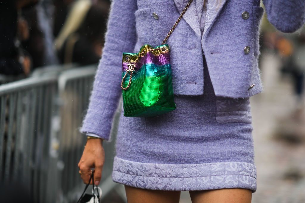 PARIS, FRANCE - OCTOBER 05: A guest wears a pale purple tweed jacket from Chanel, a matching purple tweed skirt from Chanel, a green / purple / blue / yellow sequined crossbody bag from Chanel, a white Chanel shopping bag, outside Chanel, during Paris Fashion Week - Womenswear Spring Summer 2022, on October 05, 2021 in Paris, France. (Photo by Edward Berthelot/Getty Images)