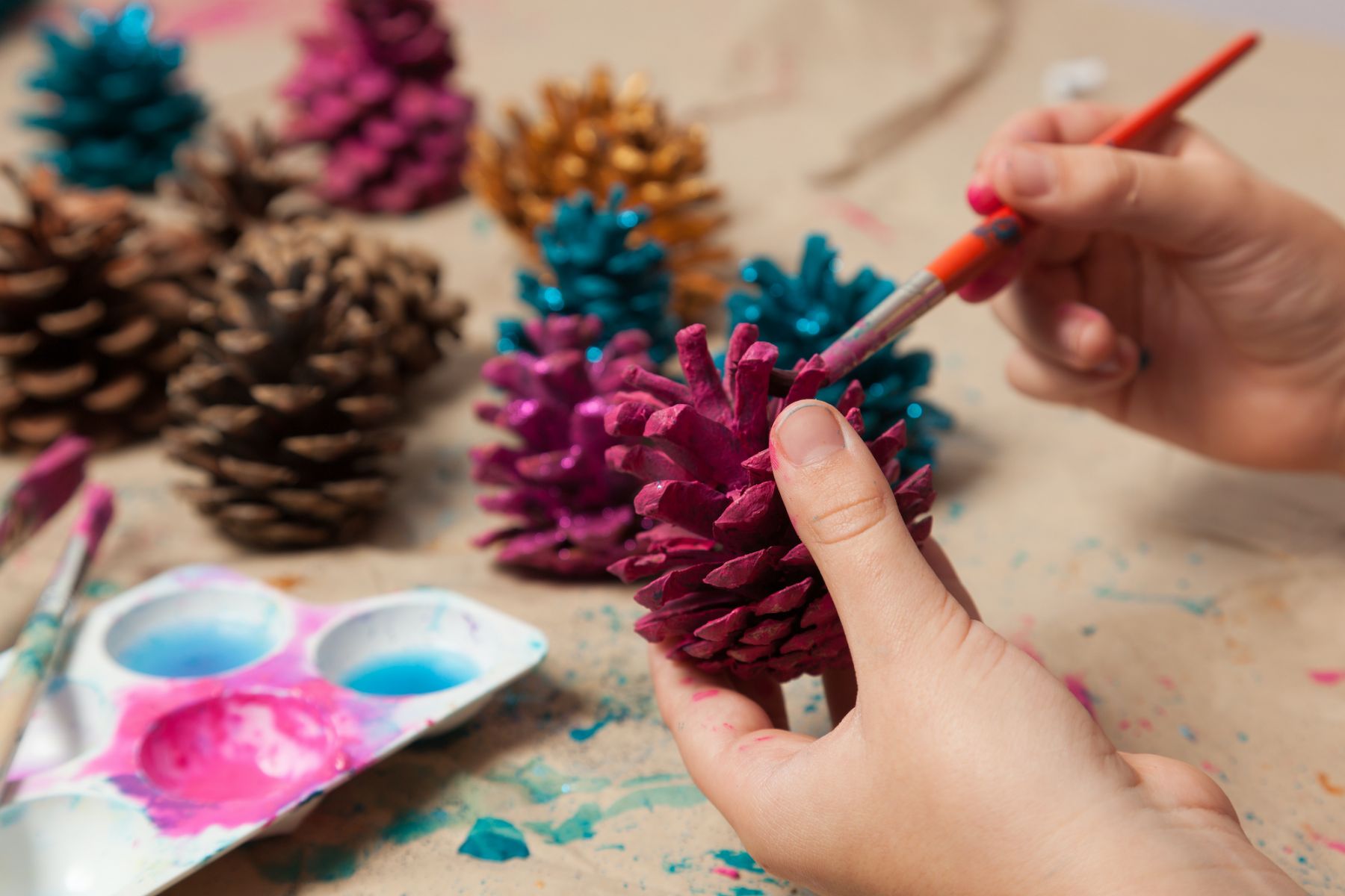 Child painting pine cones as homemade Christmas ornaments.