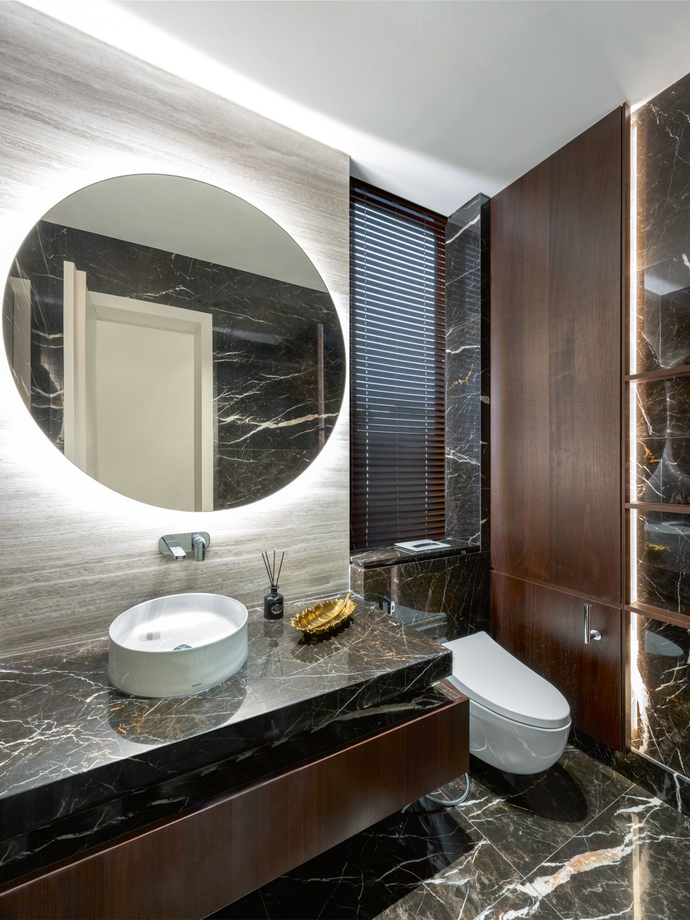 A backlit mirror catches the eye in a bathroom clad in marble tiles with dramatic veins