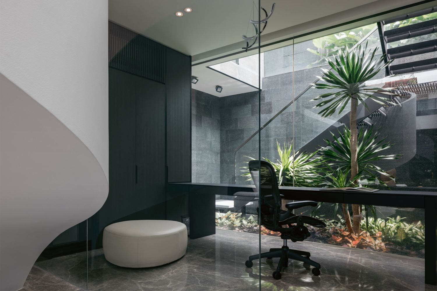 The sleek study looks out to a curved stairway and greenery in the courtyard