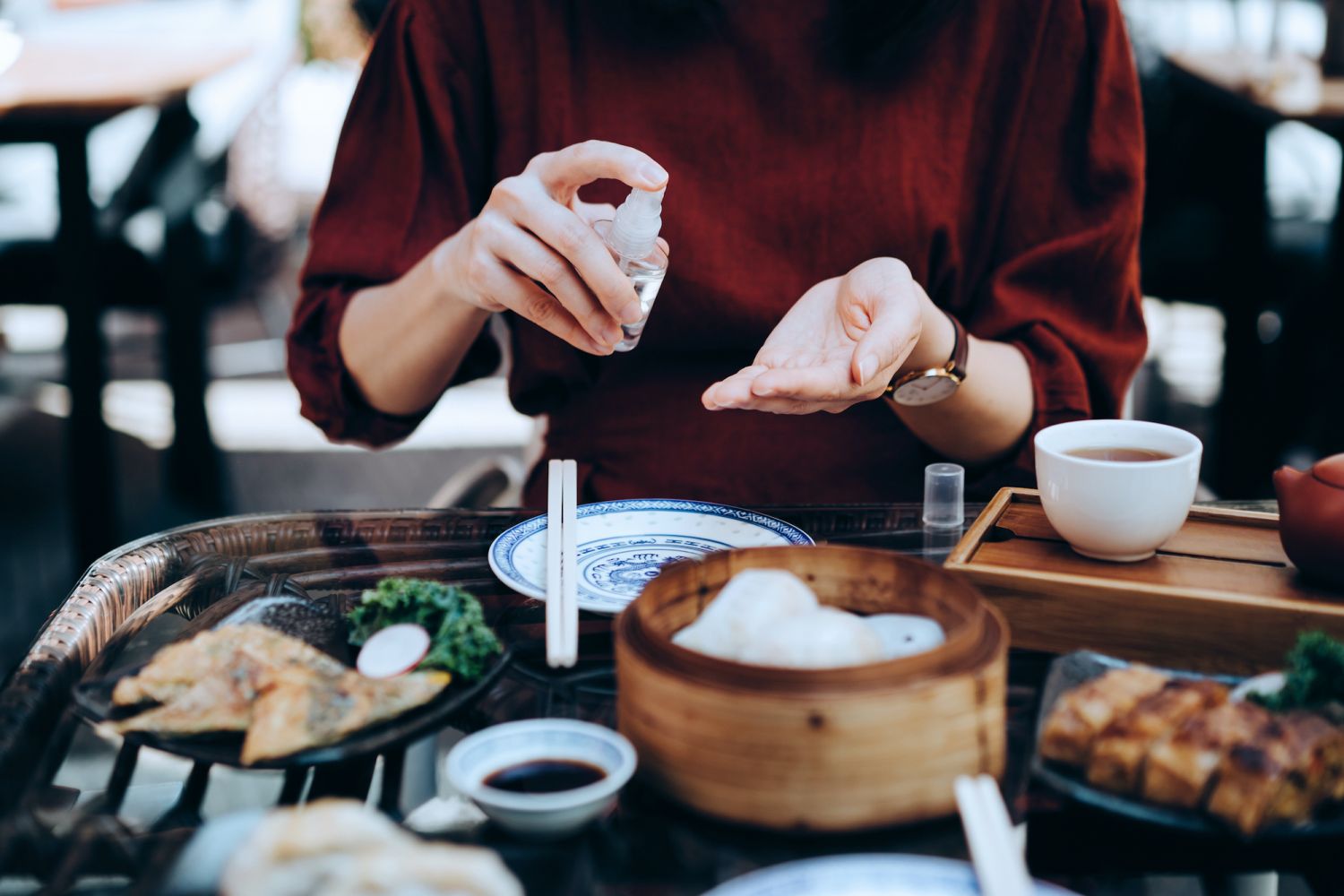 Close up of young Asian woman sanitize her hands with alcoholic sanitizer to prevent the spread of viruses before having traditional Chinese dim sum in an outdoor restaurant. Maintaining personal hygiene. The new normal of everyday life