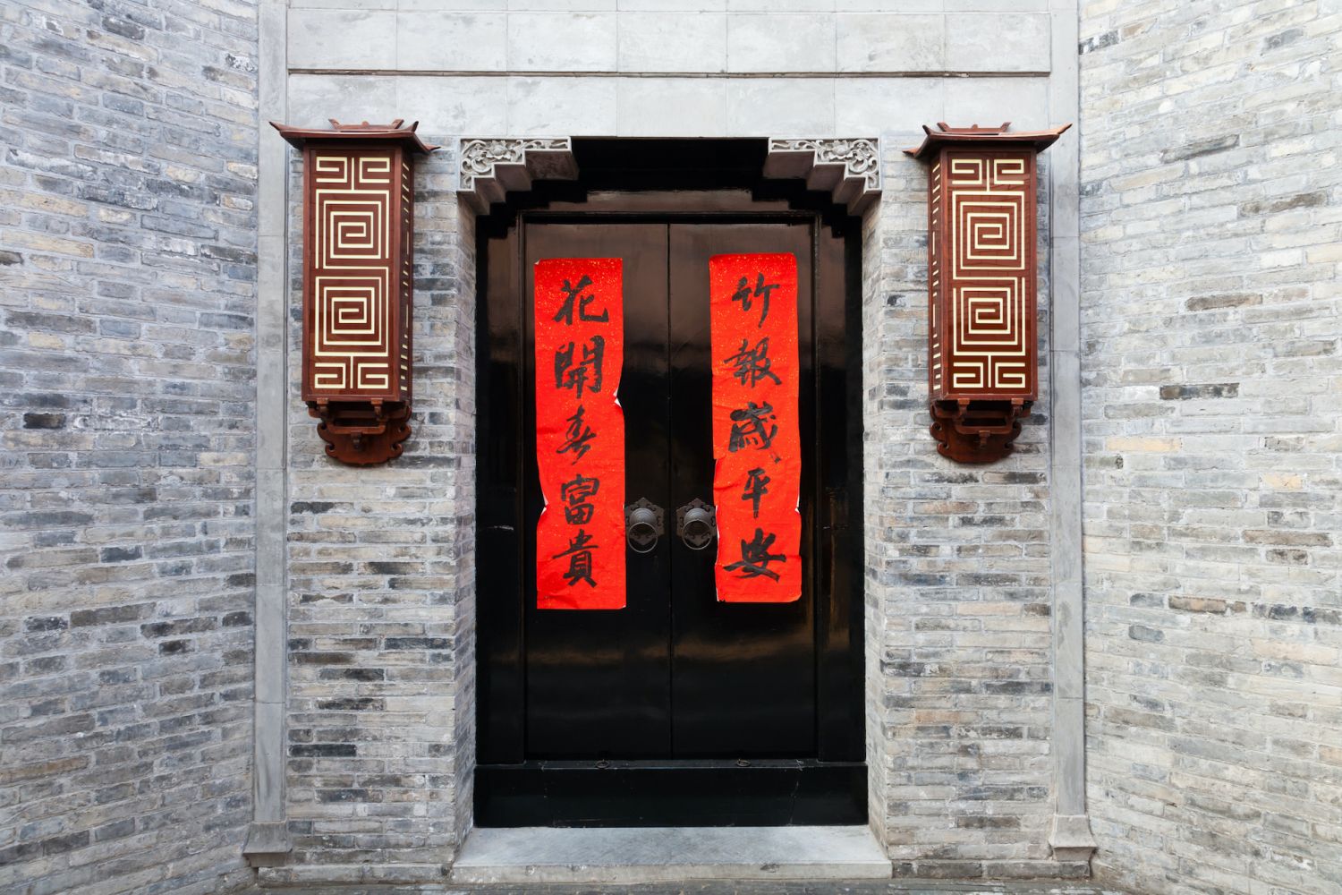 Old style architecture of gray wall and red couplet on the black door, Beijing, China. The words on couplet mean " Fortune comes with blooming flowers, family letter reports peace."