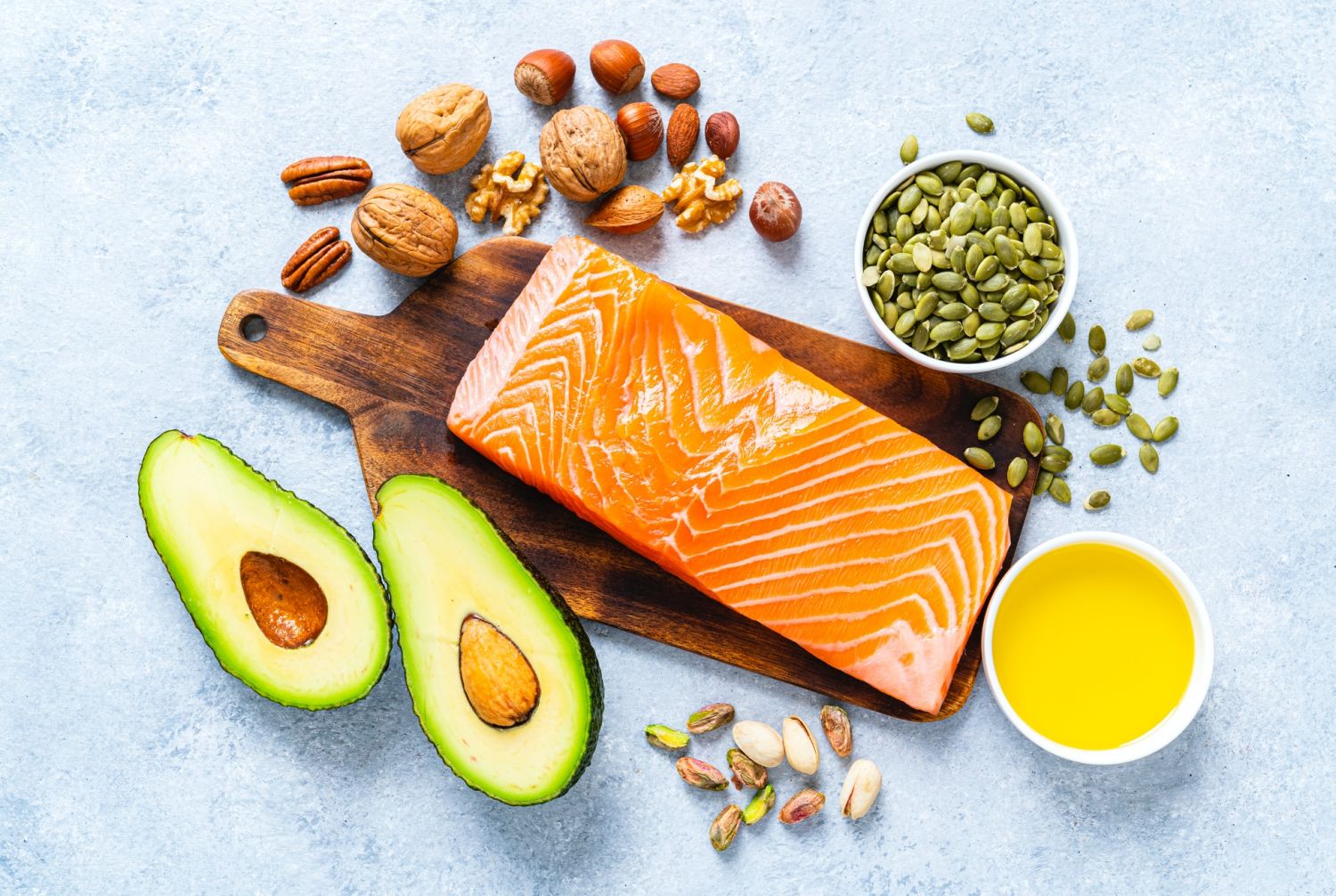 Healthy eating for well balanced diet and heart care: overhead view of a group of food rich in healthy fats. The composition includes salmon, avocado, extra virgin olive oil, nuts and seeds like walnut, almonds, pecan, hazelnuts, pistachio and pumpkin seeds. High resolution 42Mp studio digital capture taken with SONY A7rII and Zeiss Batis 40mm F2.0 CF lens