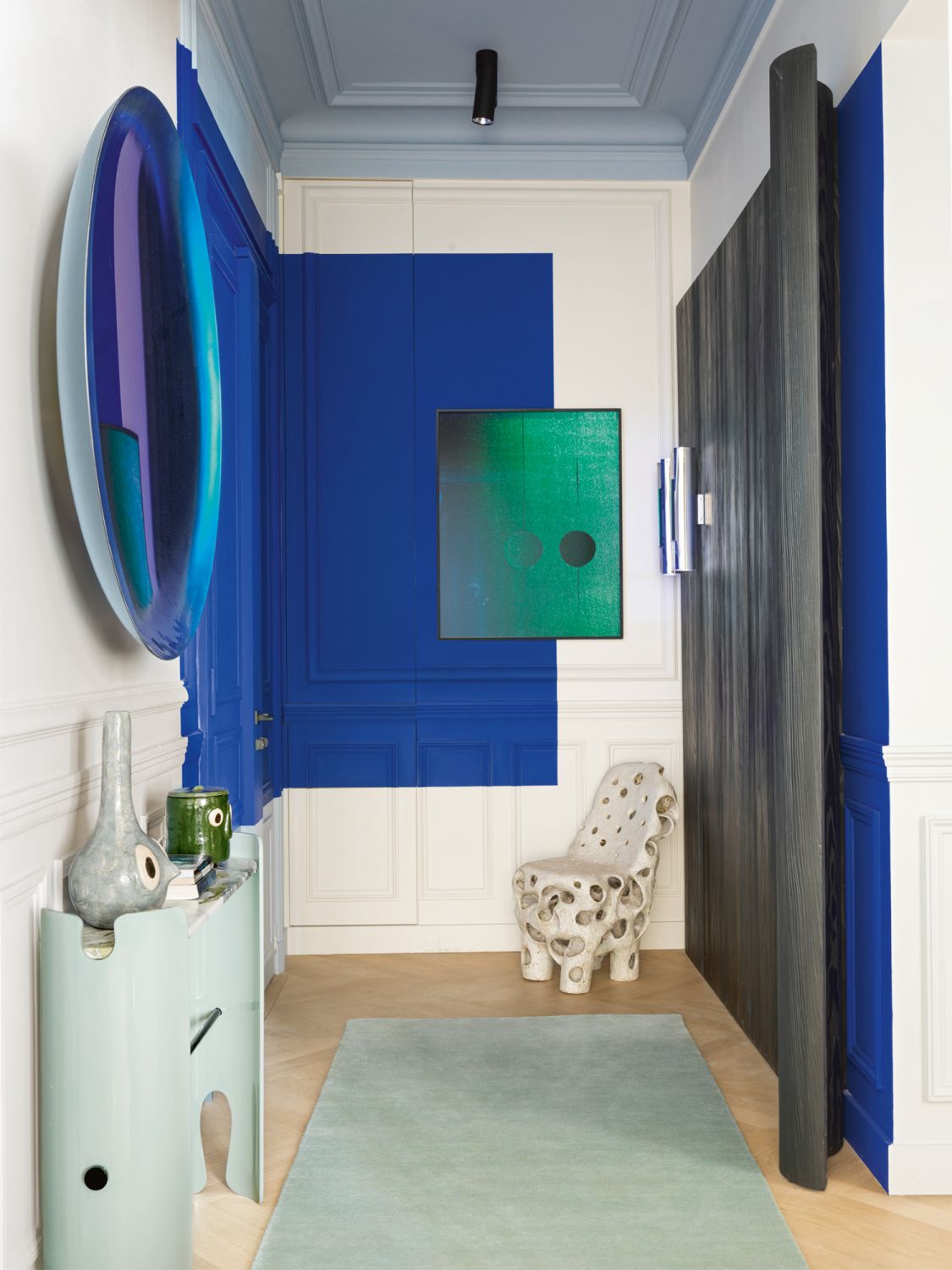 The use of blue paint on the wall echoes the hue of the wall-hung mirror by Christophe Gaignon