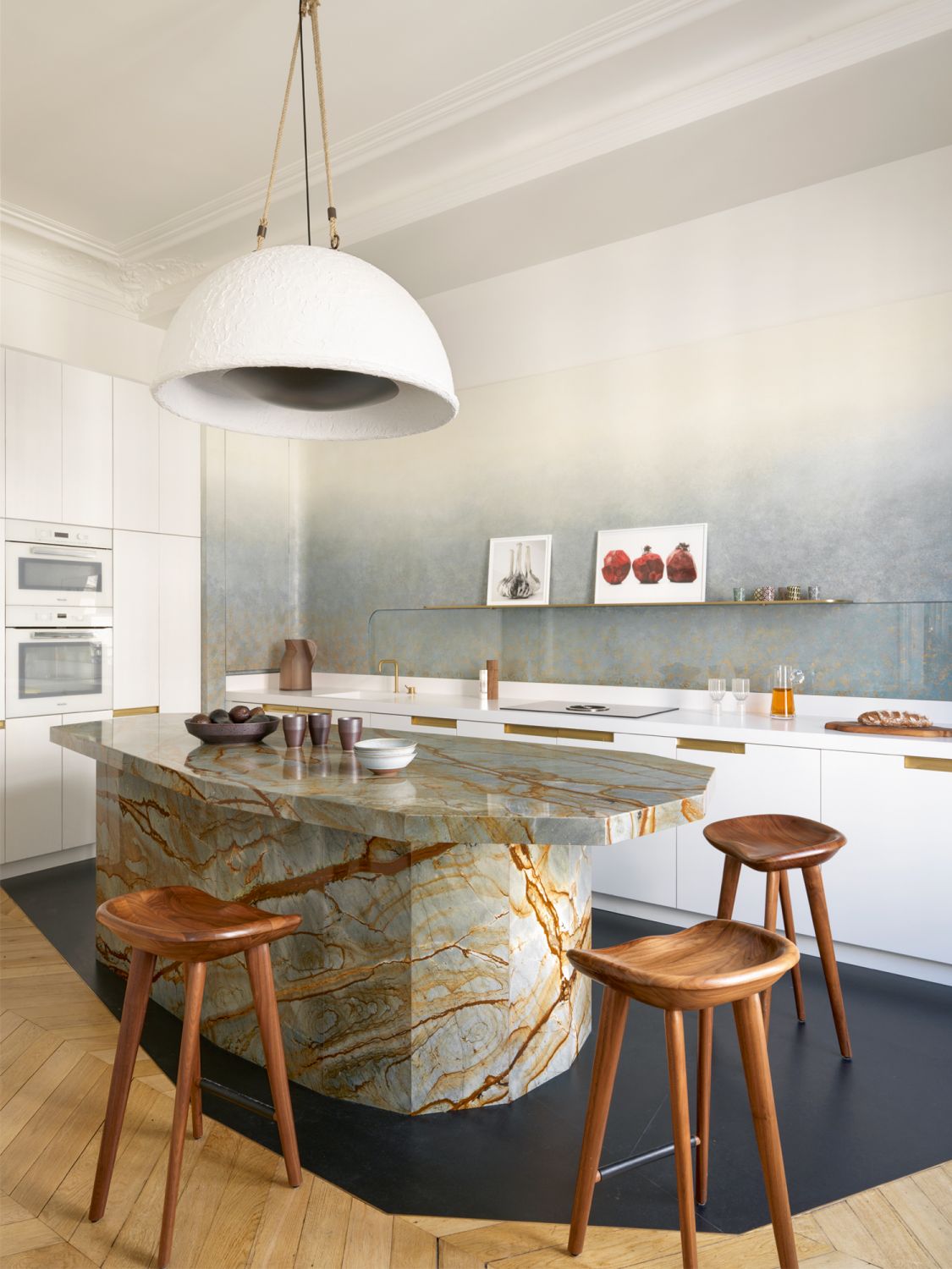 The kitchen features an eye-catching island surrounded by BassamFellows Tractor bar stools, with a Gilles & Boissier Plein Soleil light hanging overhead and an ombre wall feature by decorative painter Solène Eloy;