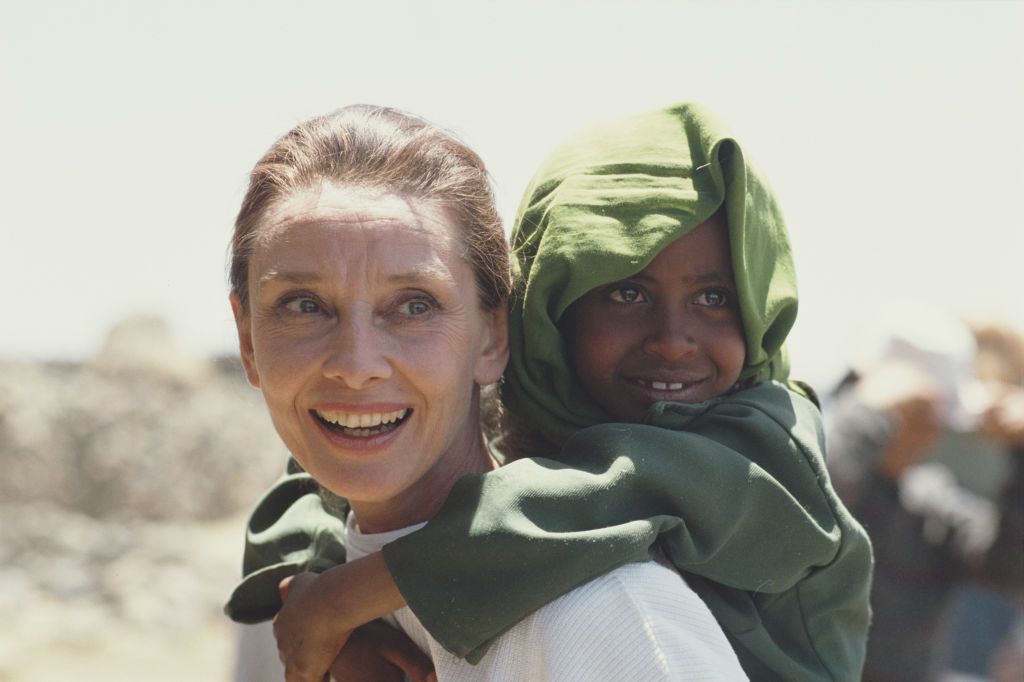 British actress and humanitarian Audrey Hepburn (1929 - 1993) carrying an Ethiopian girl on her back while on her first field mission for UNICEF in Ethiopia, 16th-17th March 1988. (Photo by Derek Hudson/Getty Images)