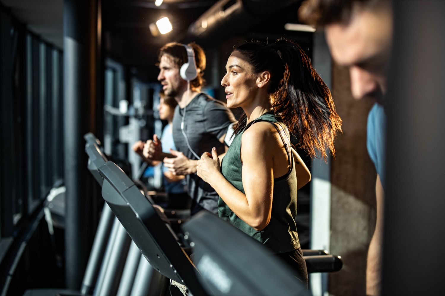 Determined athletic woman jogging on treadmill among other athletes in a gym.