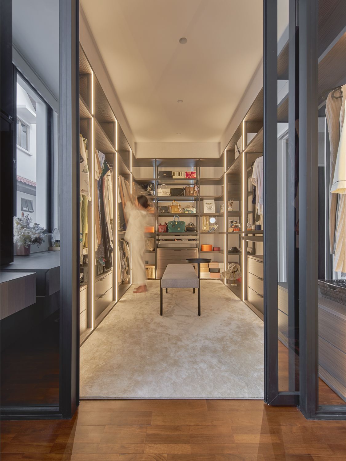 The walk-in wardrobe sports a boutique-inspired design that incorporates backlit open shelves and a bench to rest on