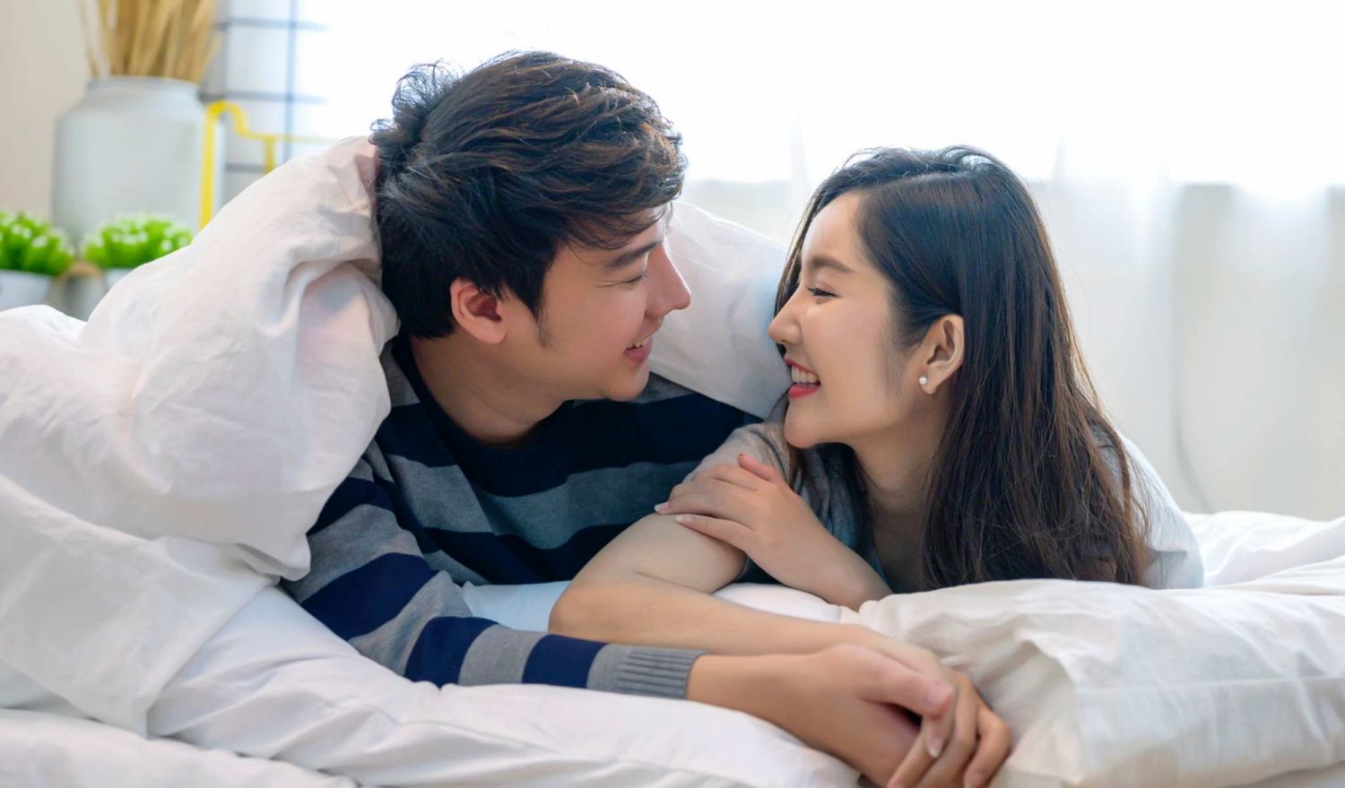 Happy young couple lying down comfortably in their bed at home. Young couple having fun lying on bed at home.