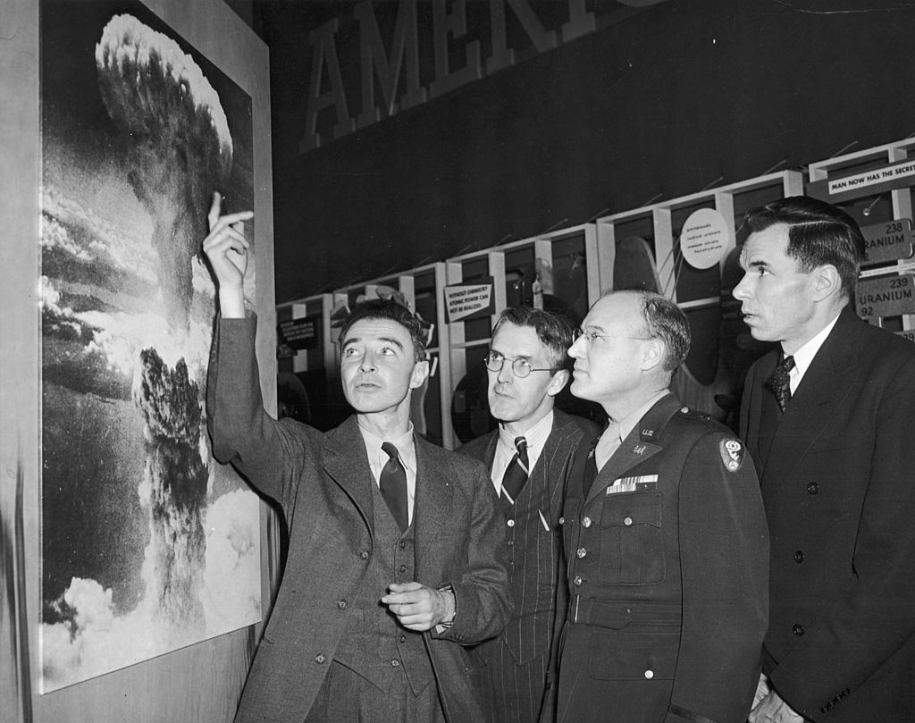 American physicist Dr. Robert Oppenheimer (1904 - 1967), points to a picture of the atomic bomb explosion over Nagasaki, Japan, as scientist Henry D. Smyth (1898 - 1986) (second left), major General Kenneth D. Nichols (1907 - 2000) (second right), and scientist Glenn Seaborg (1912 - 1999) look on, 1940s. (Photo by Hulton Archive/Getty Images)