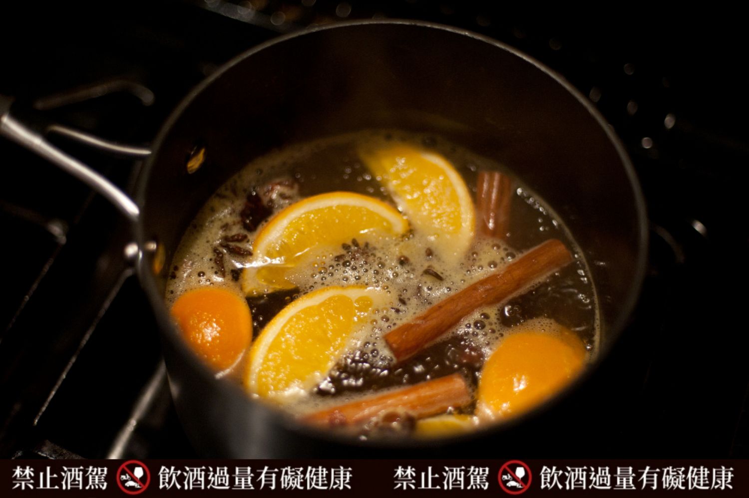 White wine being mulled in a saucepan on a stove, with cinnamon, oranges, cloves and star anise.